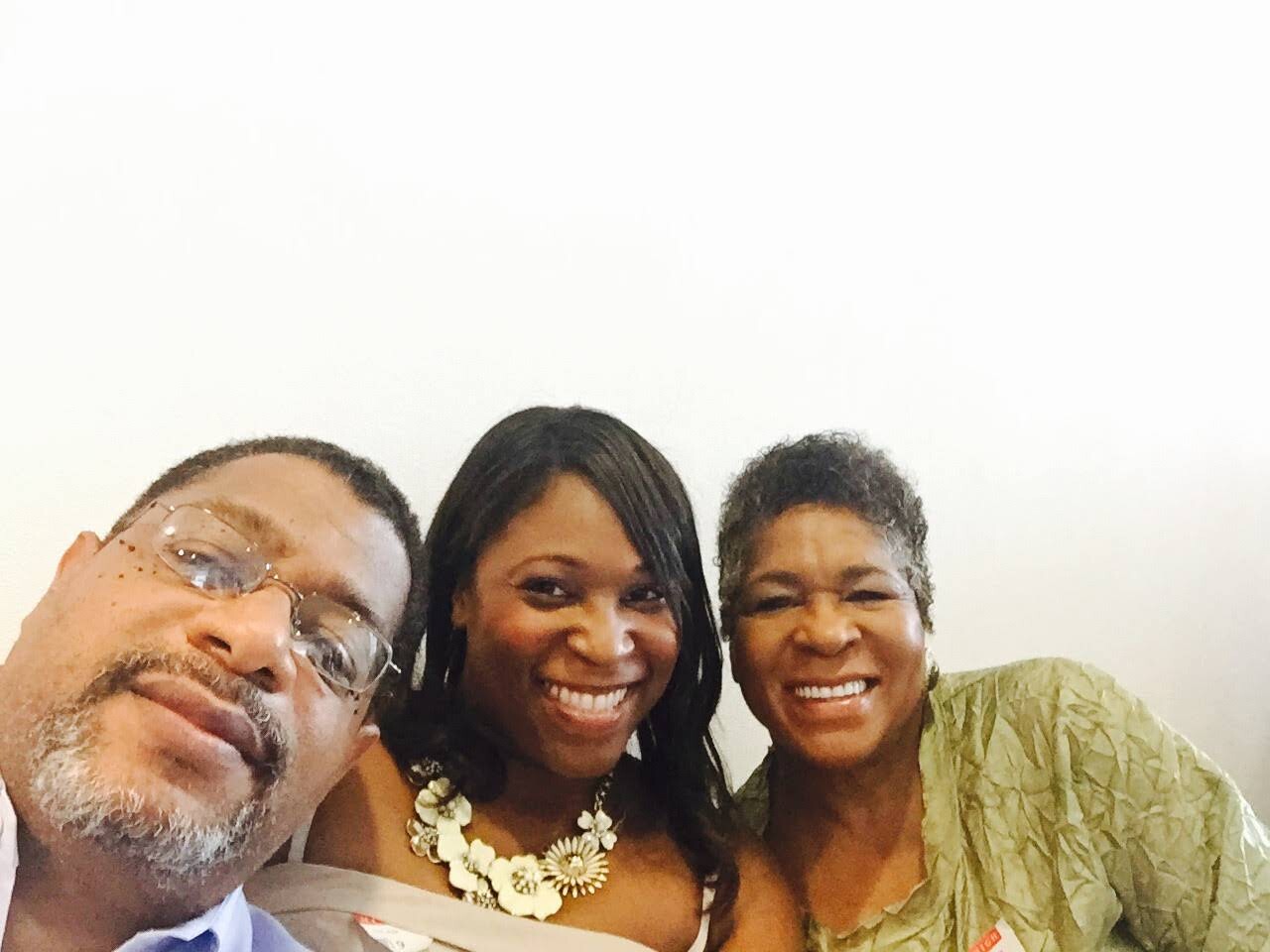 Three friends taking a cheerful selfie, smiling at the camera against a plain light background.