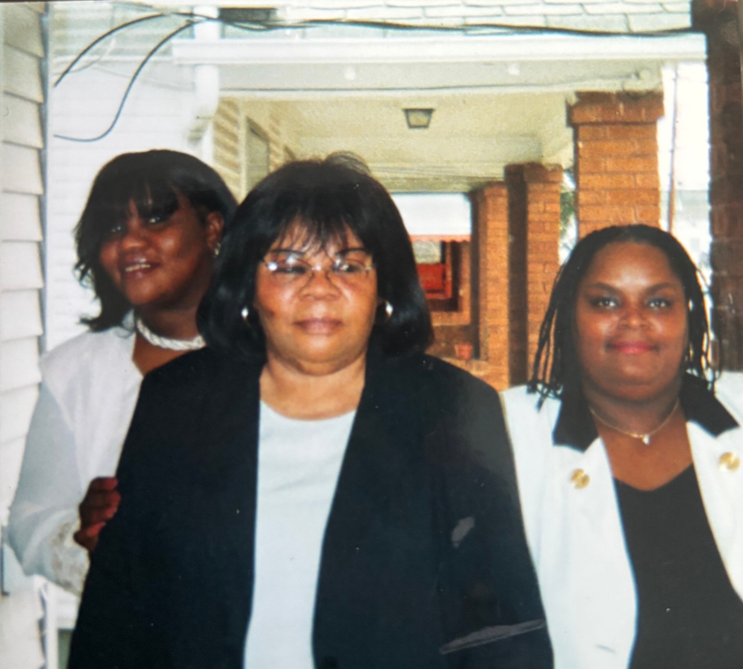 Three women posing for a group photo outdoors, dressed in formal outfits.