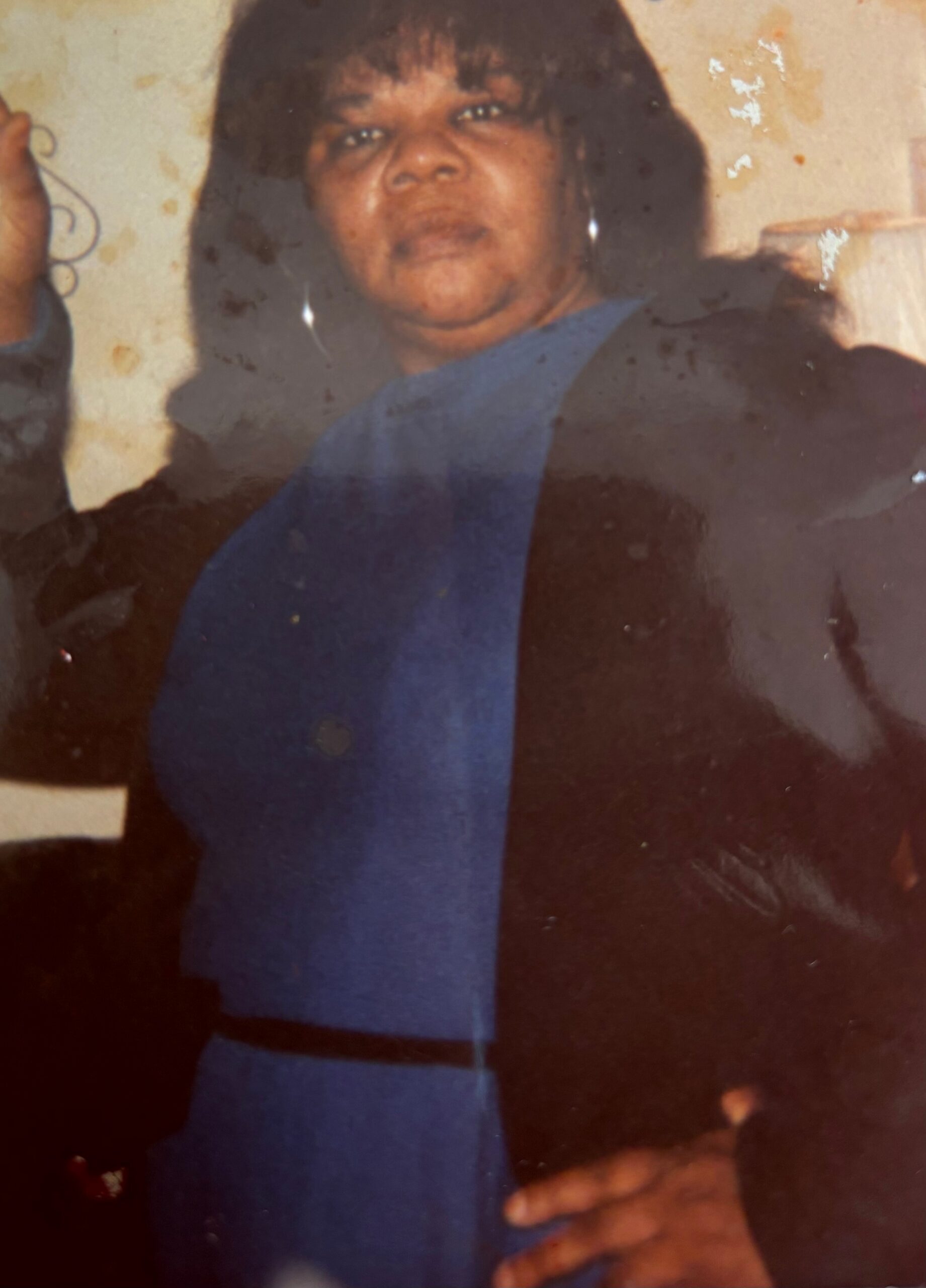 Portrait of a woman with dark hair wearing a blue top, looking toward the camera in a faded, stained photograph.