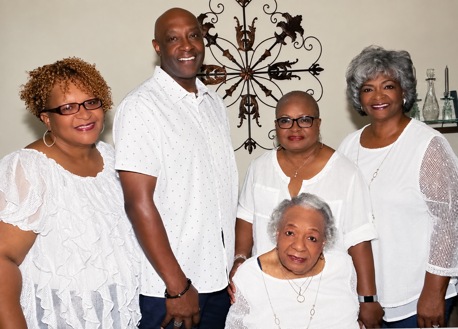 Five adults posing together indoors, all wearing white tops and smiling at the camera.