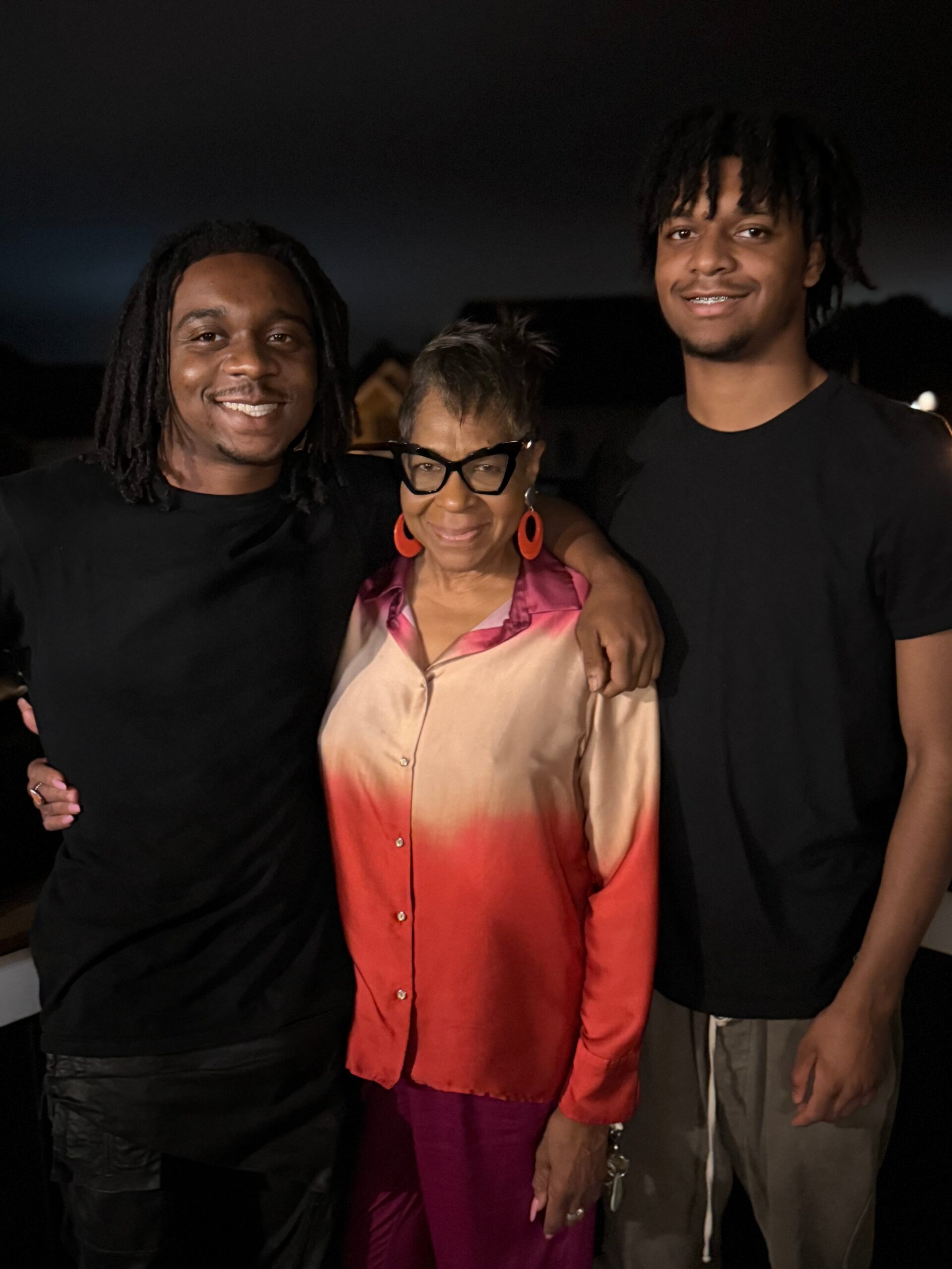 Three people posing together at night, smiling, with arms around each other.