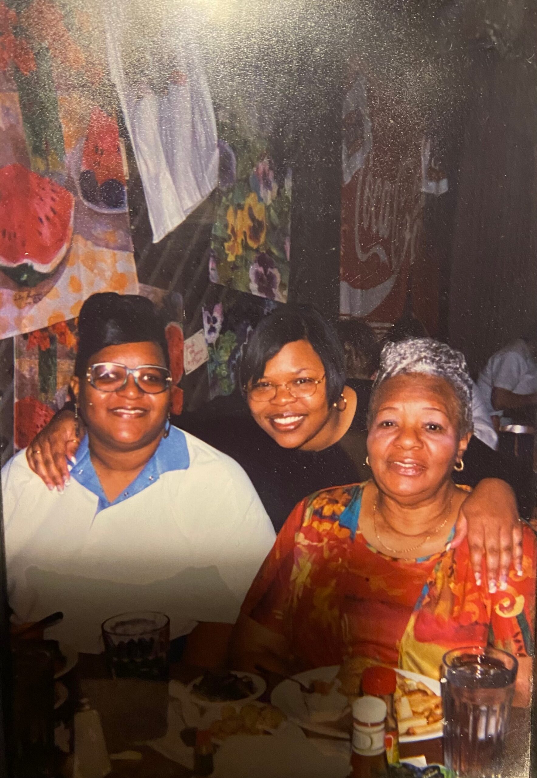 Three smiling women sit at a table with plates and drinks during a celebration outside the frame of the photo's edge.