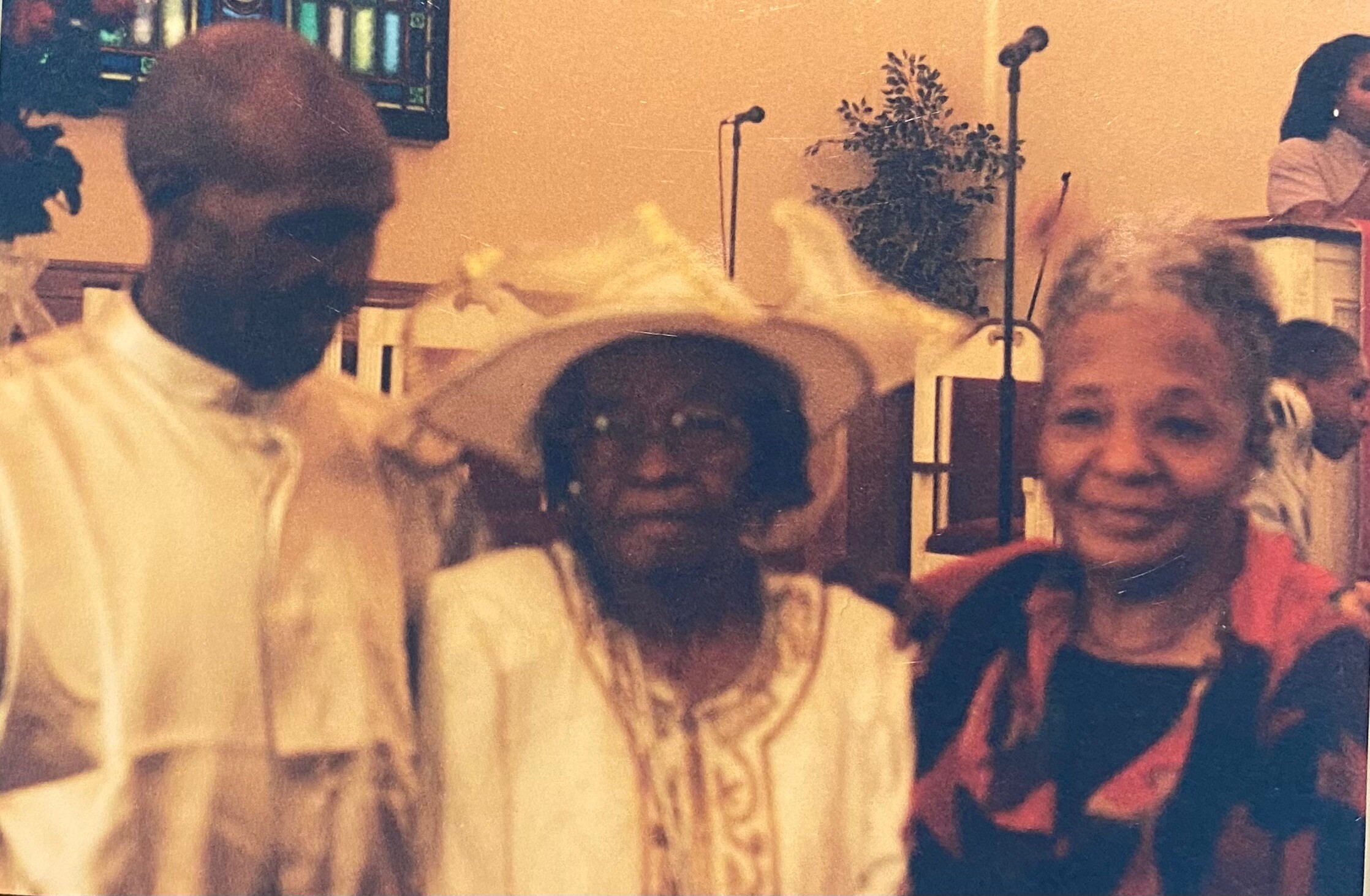 Three people posing for a photo at a social event, with microphones and a plant visible in the background.