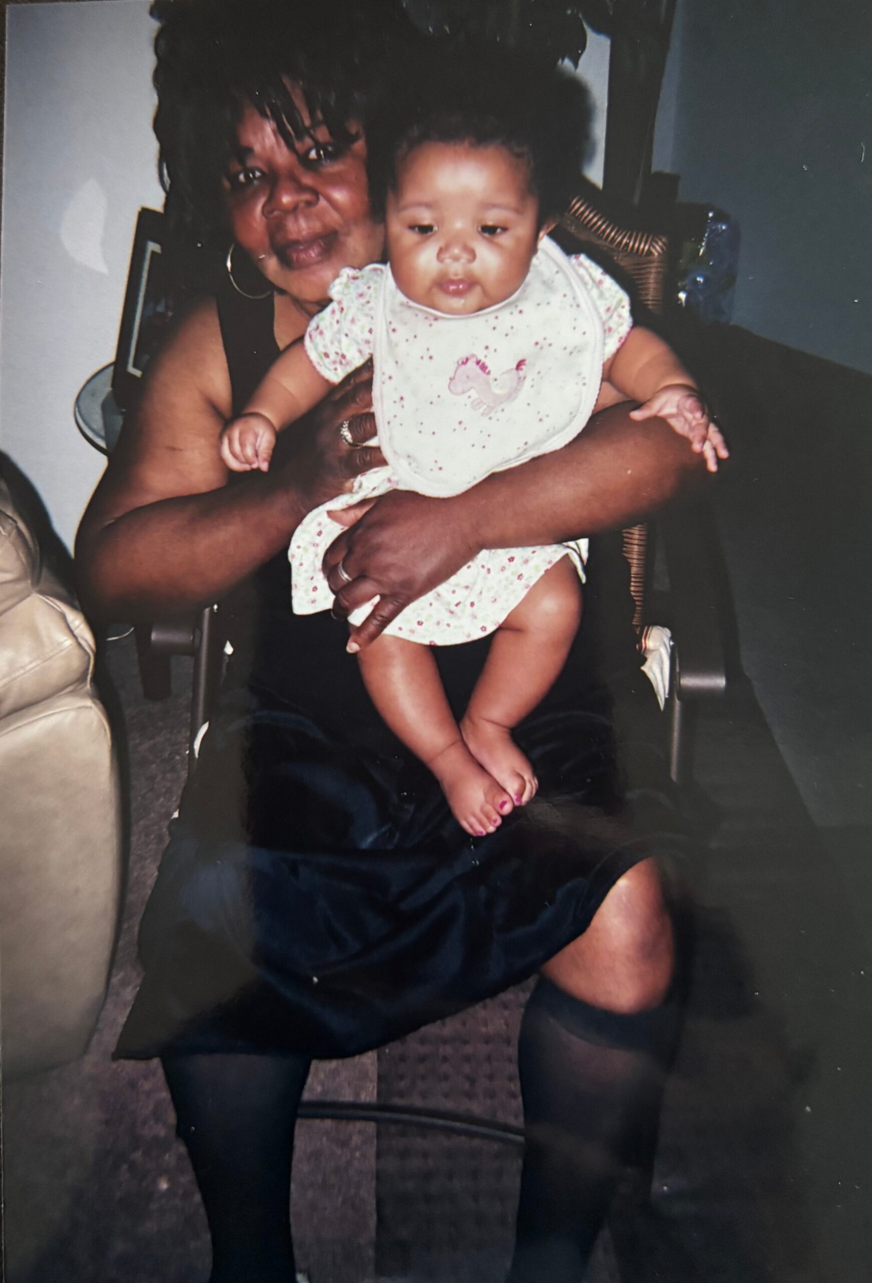 Woman with hoop earrings cradling a baby on her lap indoors; baby wears a white bib with a pink unicorn design.