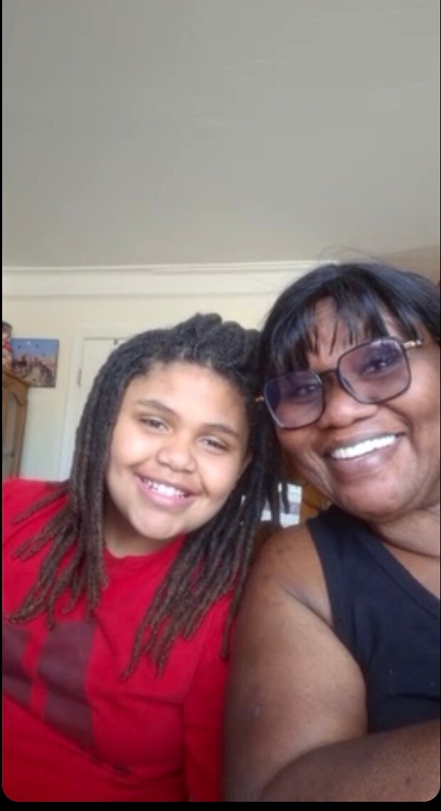 Two smiling people taking a selfie indoors—a woman with glasses and a child with braids, both facing the camera.