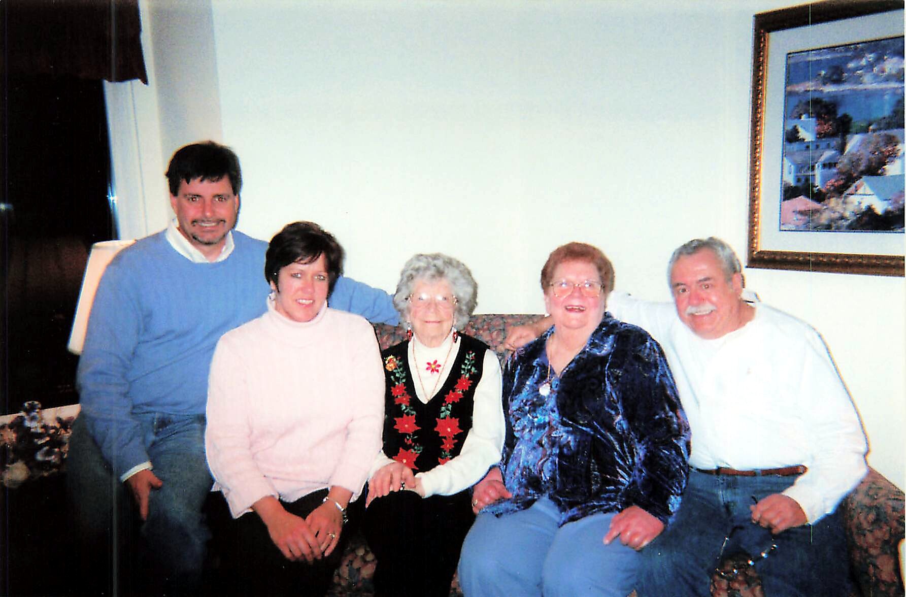 Five people sit closely together on a sofa in a living room, smiling for a group photo.