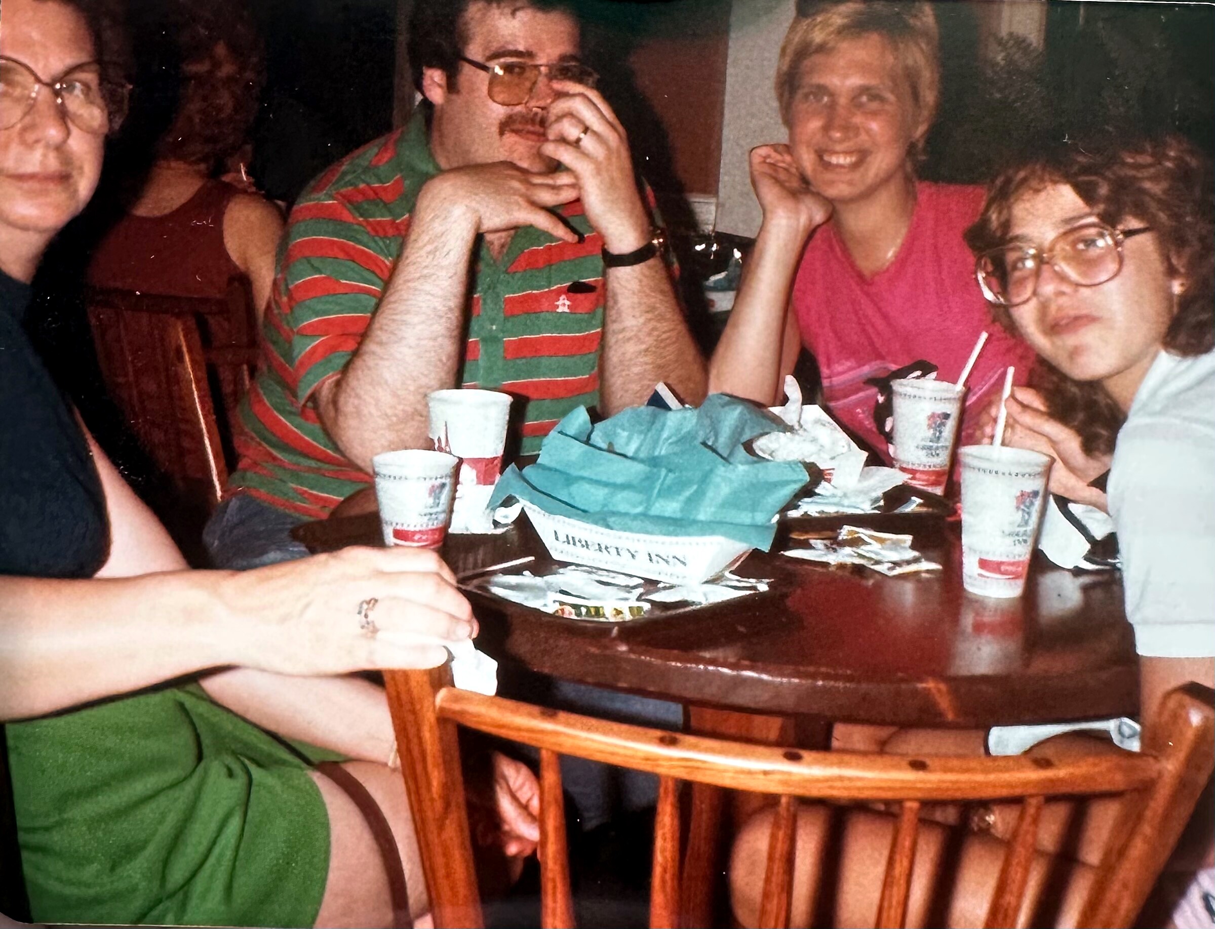 Group of friends seated around a table with cups and crumpled napkins, smiling and talking.