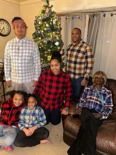 Multigenerational family posing in a living room with a Christmas tree; everyone wears plaid shirts.