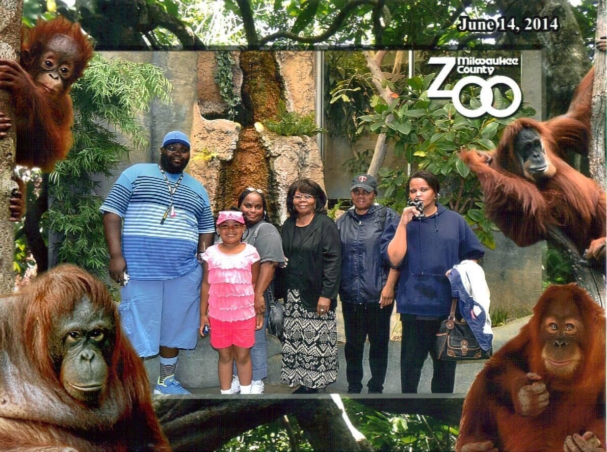 Group of seven adults and one child posing for a photo in an orangutan exhibit at Milwaukee County Zoo (June 14, 2014).