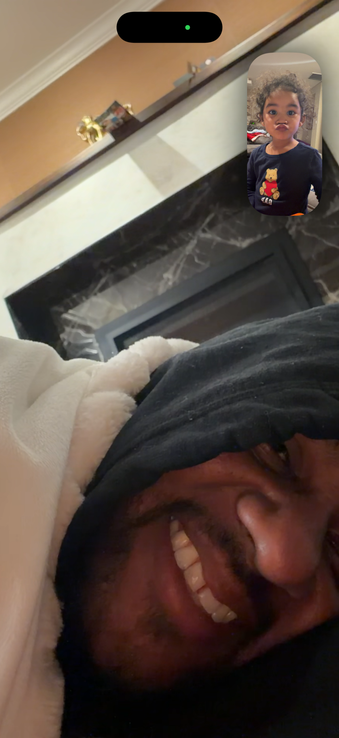 Person smiling in bed with a white blanket; inset video call shows a child puckering lips.