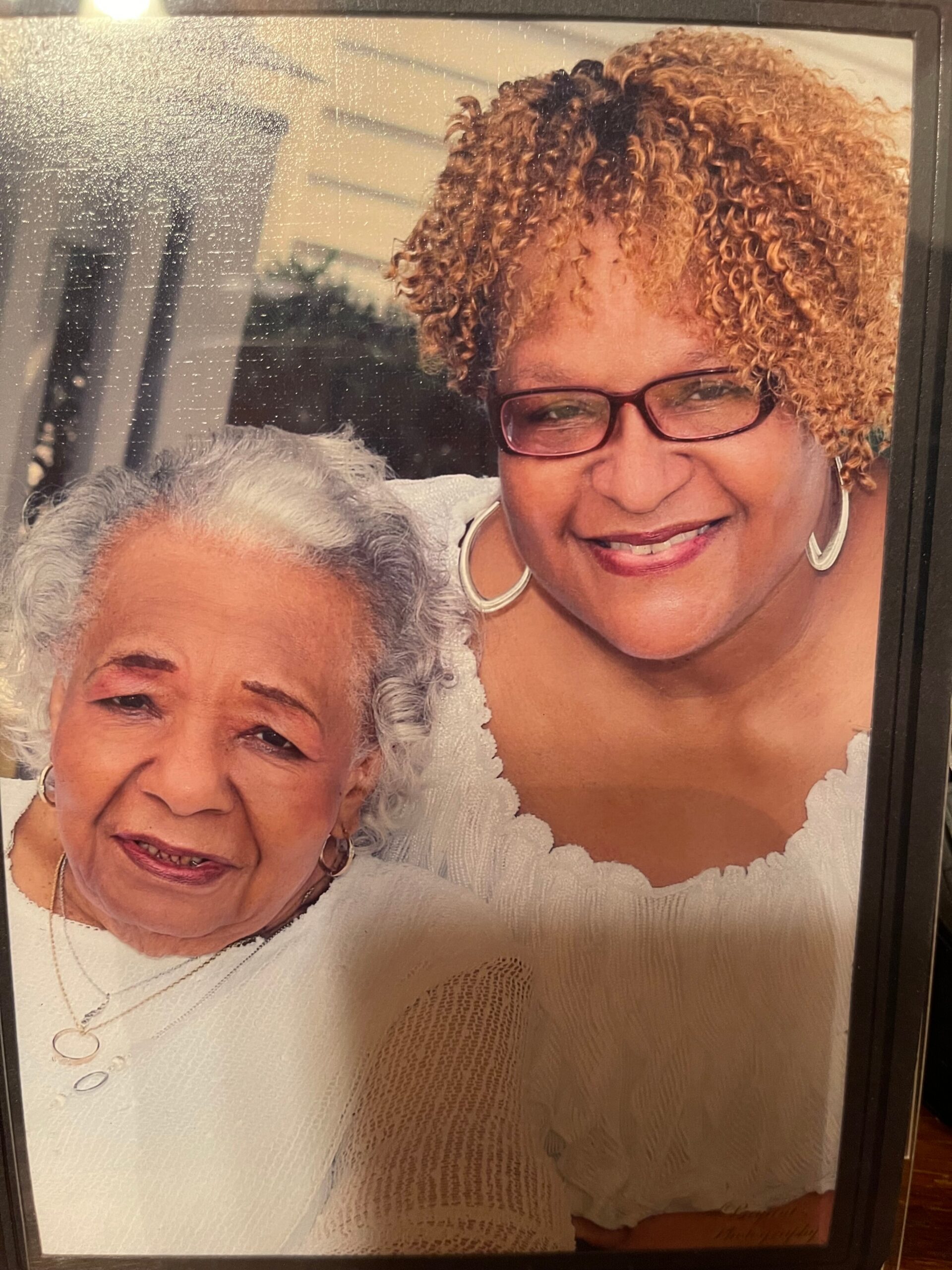 Framed photo of two smiling women, an elderly woman with gray hair on the left and a younger woman with curly hair and glasses on the right.