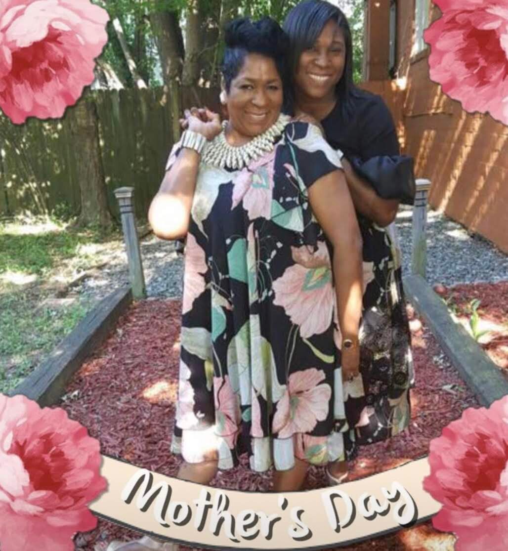 Two women posing together outdoors, one wearing a floral dress and chunky necklace, smiling for a Mother's Day photo.