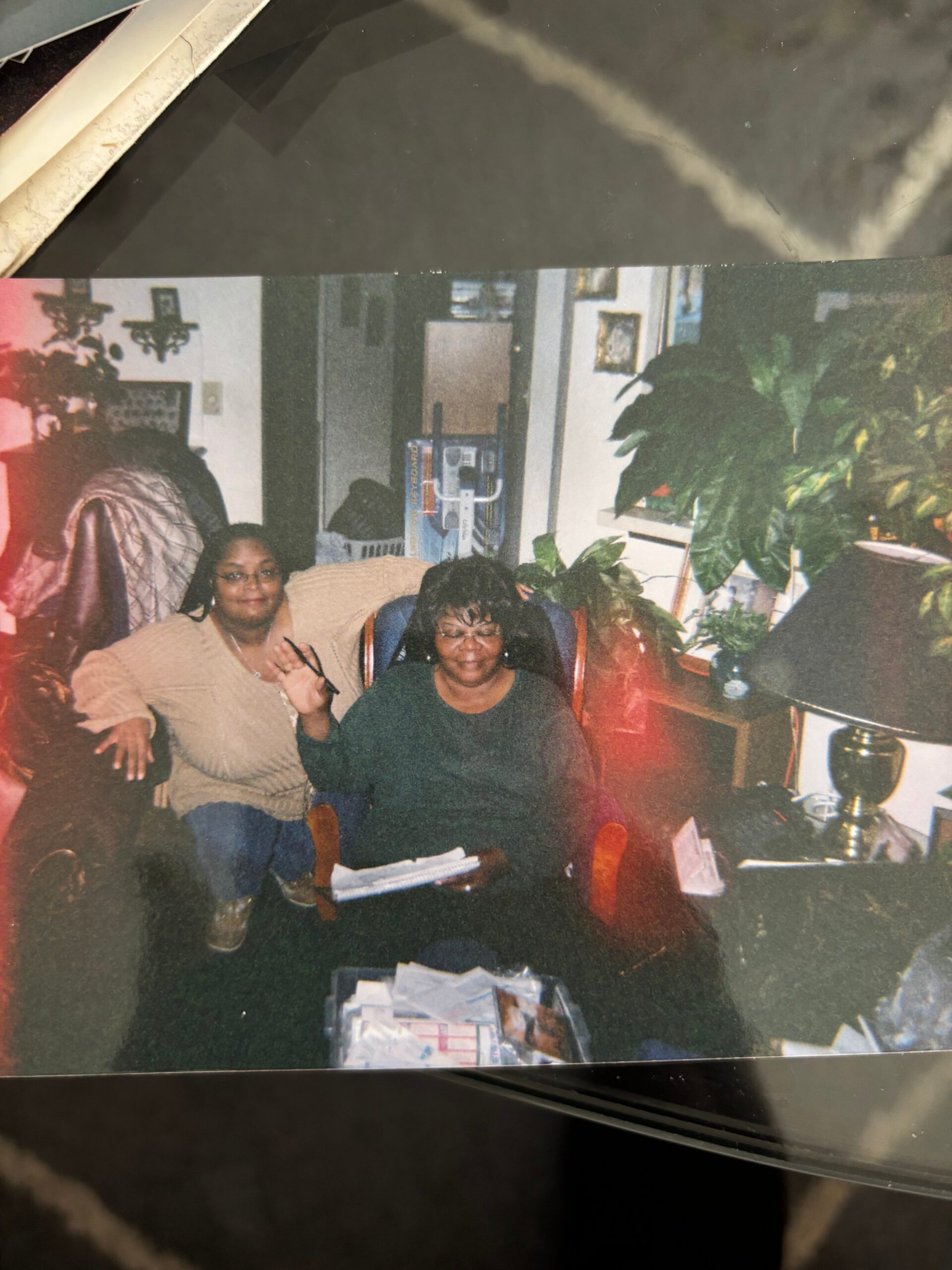 Two women sitting in a cozy living room, smiling for the photo, with plants and furniture around them.