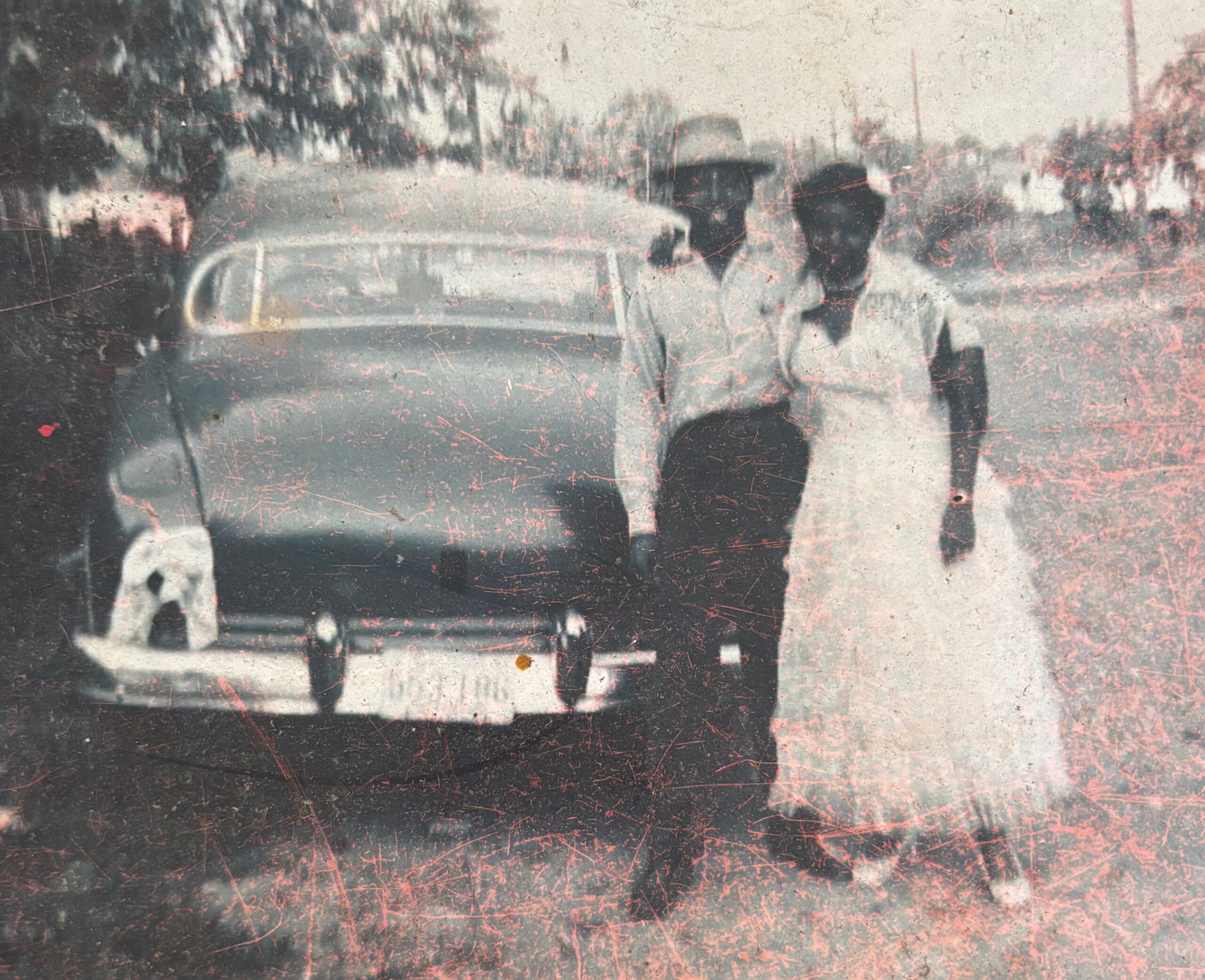 Grayscale, distressed photograph of people walking on a street near a vintage car.