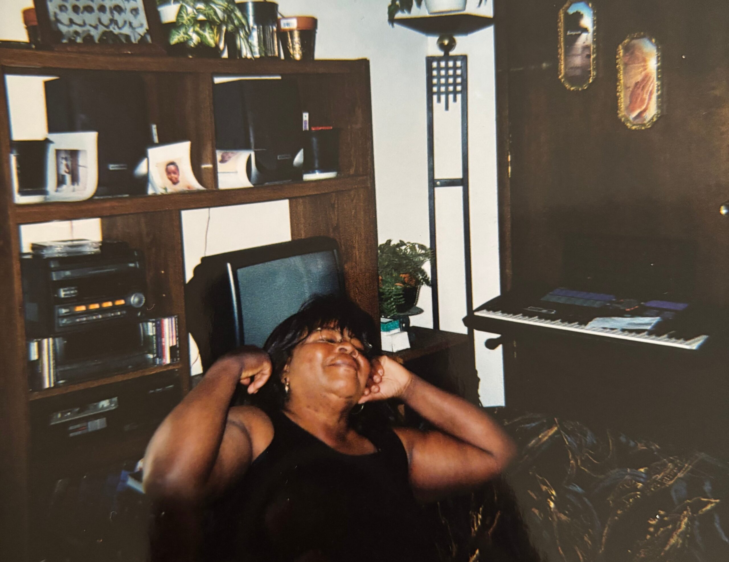 Person asleep on the floor, head resting on arms, in a living room with a wooden cabinet, computer keyboard, and decor in the background.