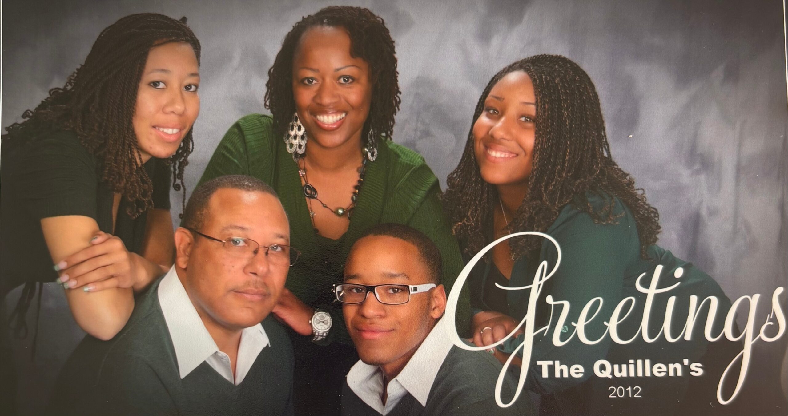 Five people—three women and two men—smiling together for a group portrait against a dark backdrop, dressed in green and white accents.