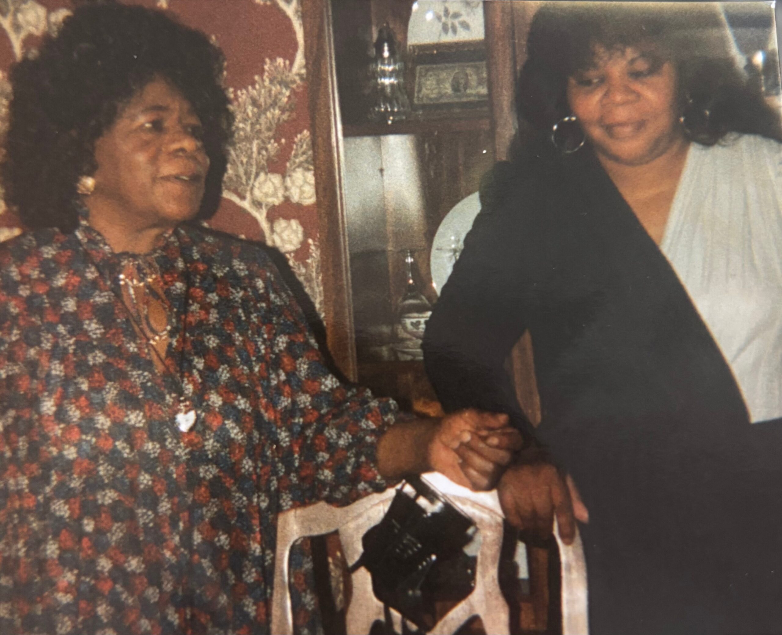 Two older women sit together at a table, smiling during a family gathering in a cozy home setting.
