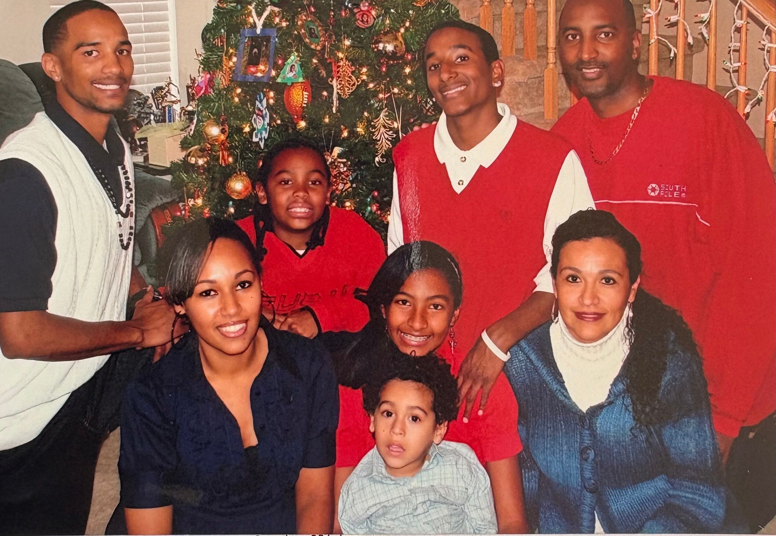 A multi‑generational family poses together for a holiday photo in front of a decorated Christmas tree, smiling at the camera.