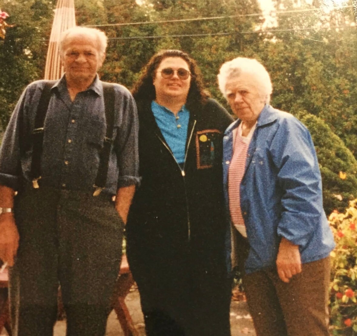 Three adults standing together outdoors in a garden, smiling.