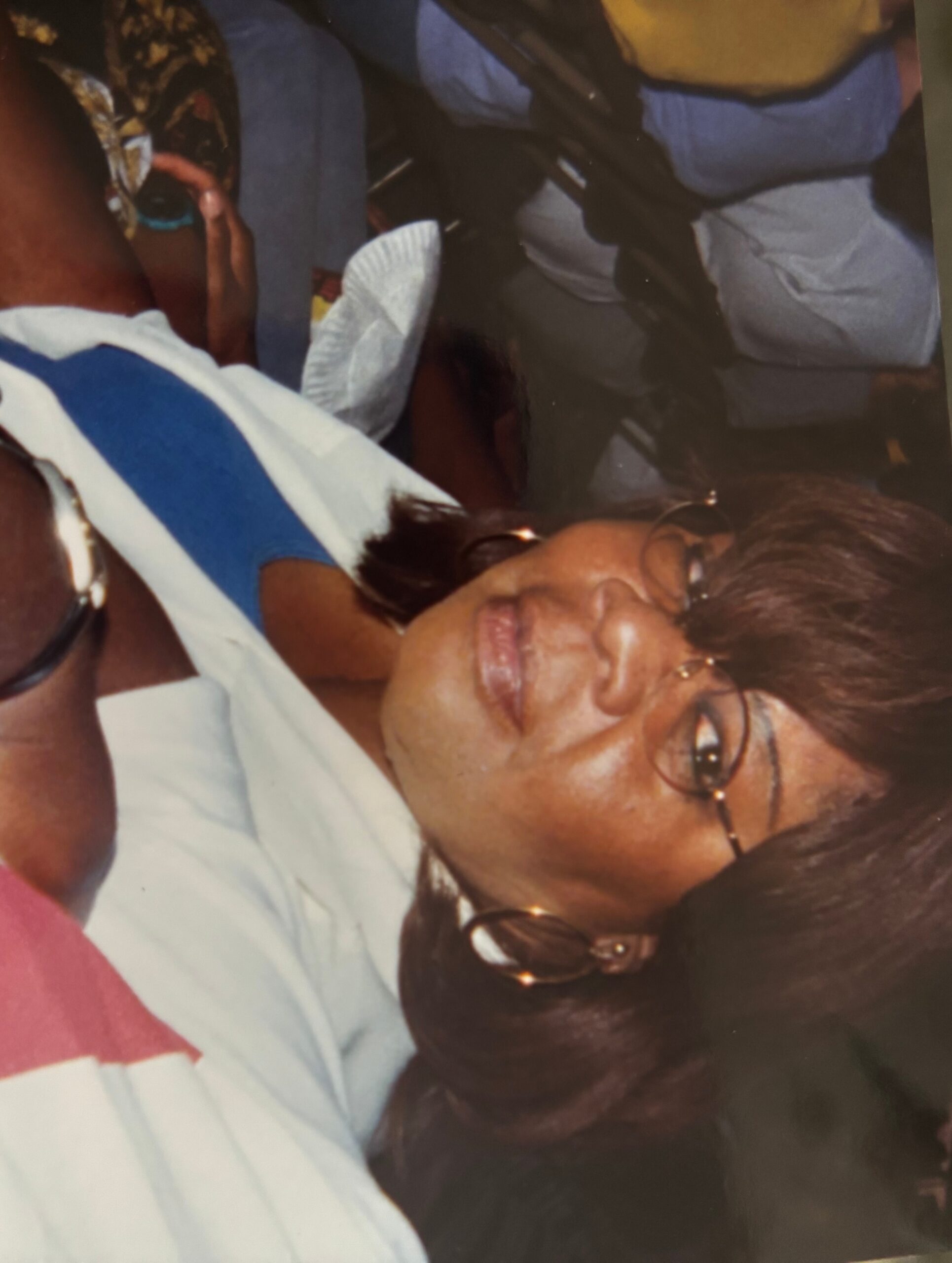 Smiling woman with short dark hair and glasses, wearing a light blue shirt and hoop earrings.