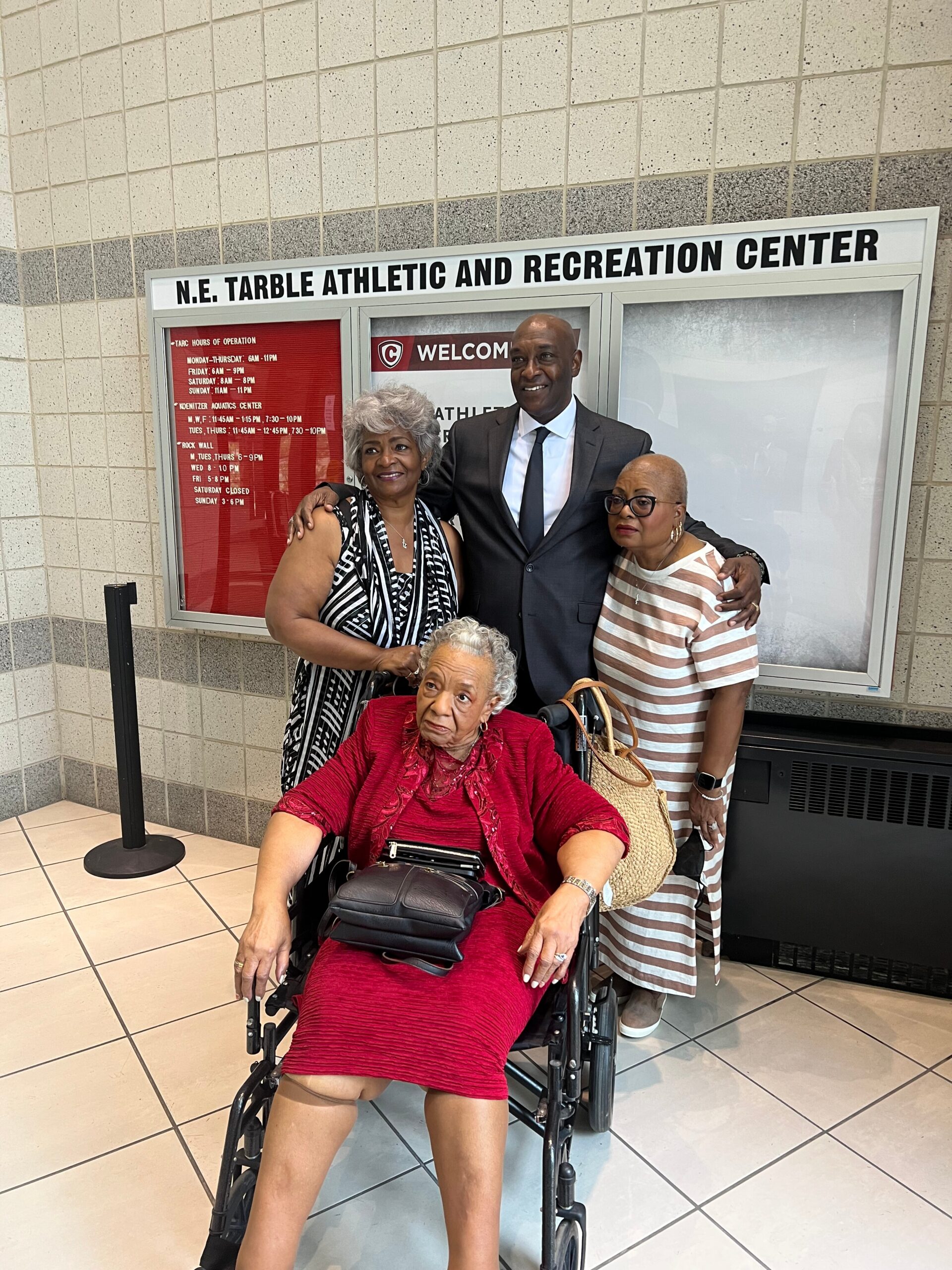 Group of four posing in a recreation center lobby, with a woman in a red dress in a wheelchair in the foreground.