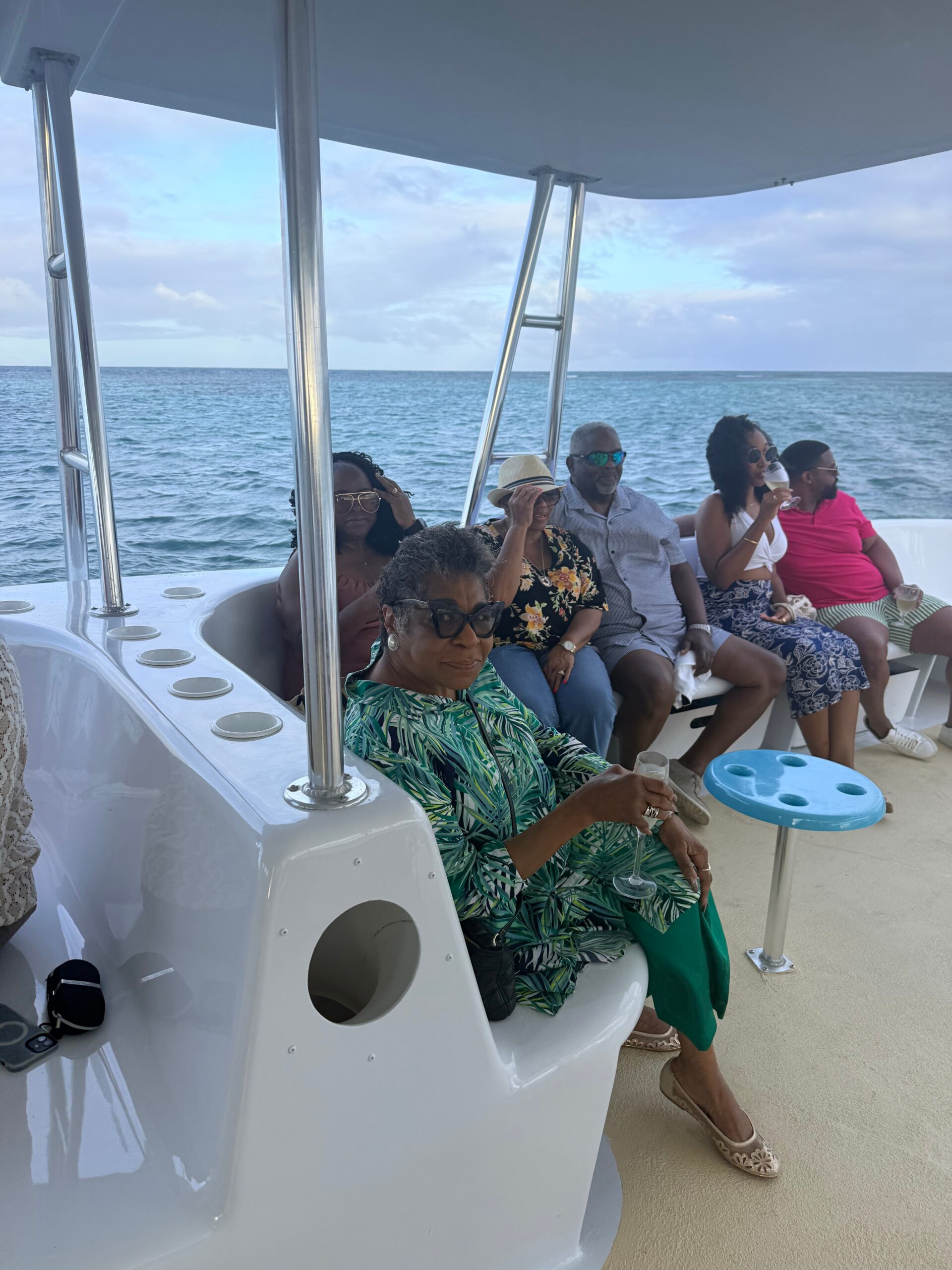 Group of adults relaxing on a white boat deck, sipping drinks as the blue ocean stretches to the horizon.