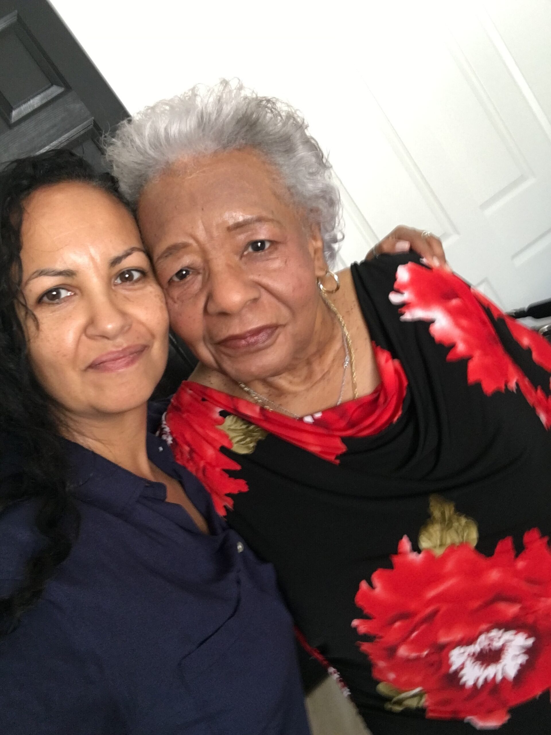 Two women posing for a selfie: younger with dark hair on left, older with gray hair and red floral scarf on right.