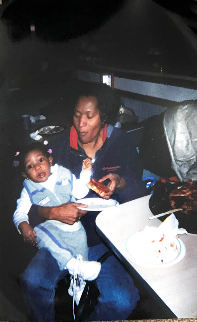 Woman feeding a young child a slice of pizza at a table with pizza plates nearby in a dimly lit setting, sharing a meal together.