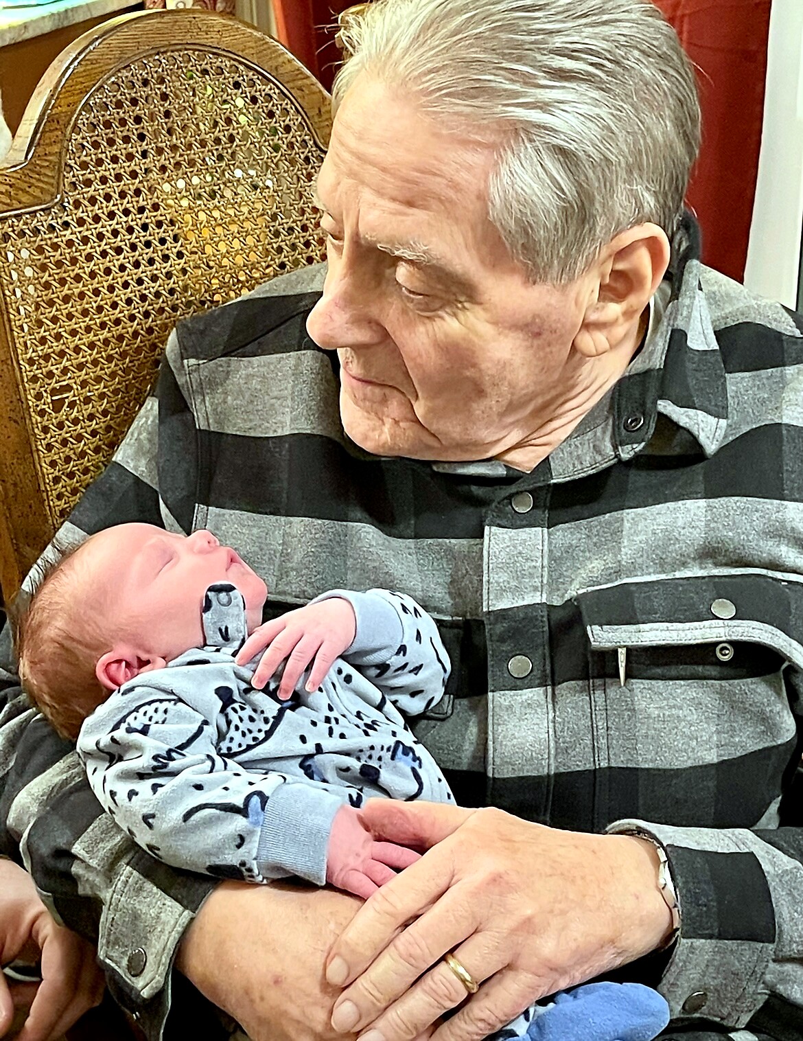 Older man in a plaid shirt holding a newborn baby, gazing down with affection.