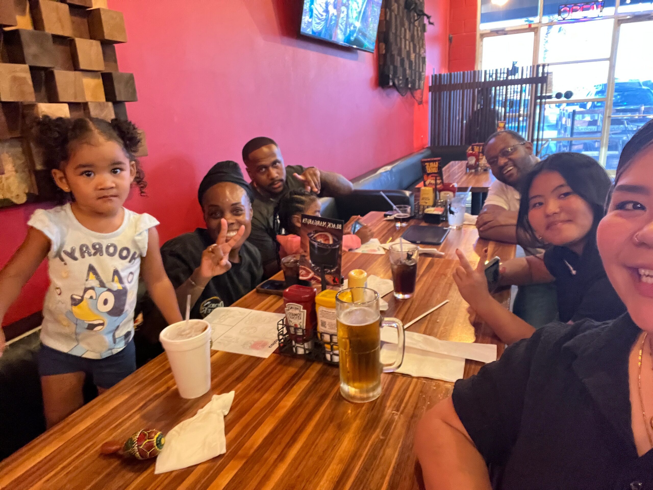 Group of people around a wooden restaurant table posing for a photo with drinks and condiments visible.