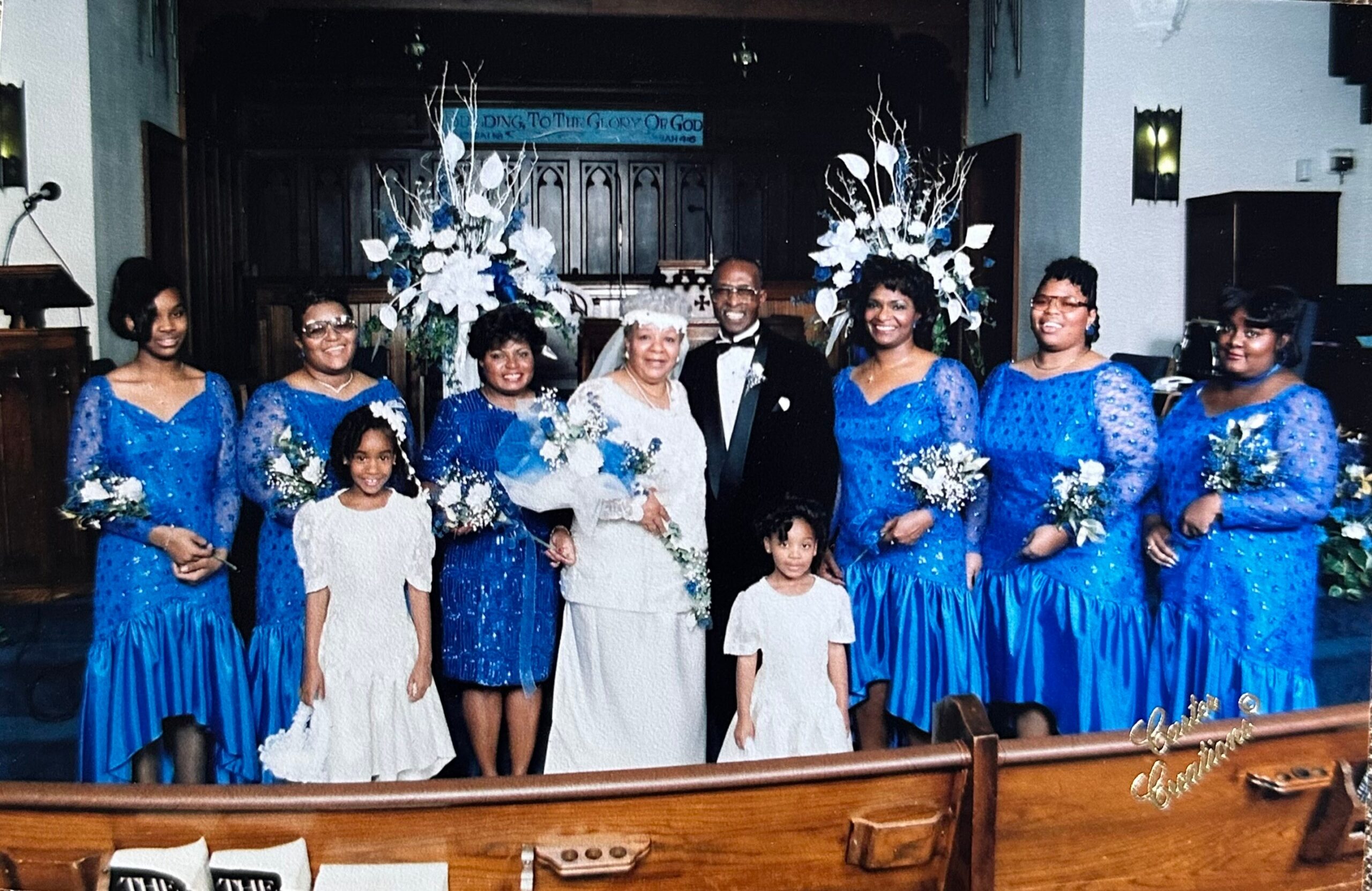 Bride and groom center stage, flanked by bridesmaids in blue dresses inside a church sanctuary.