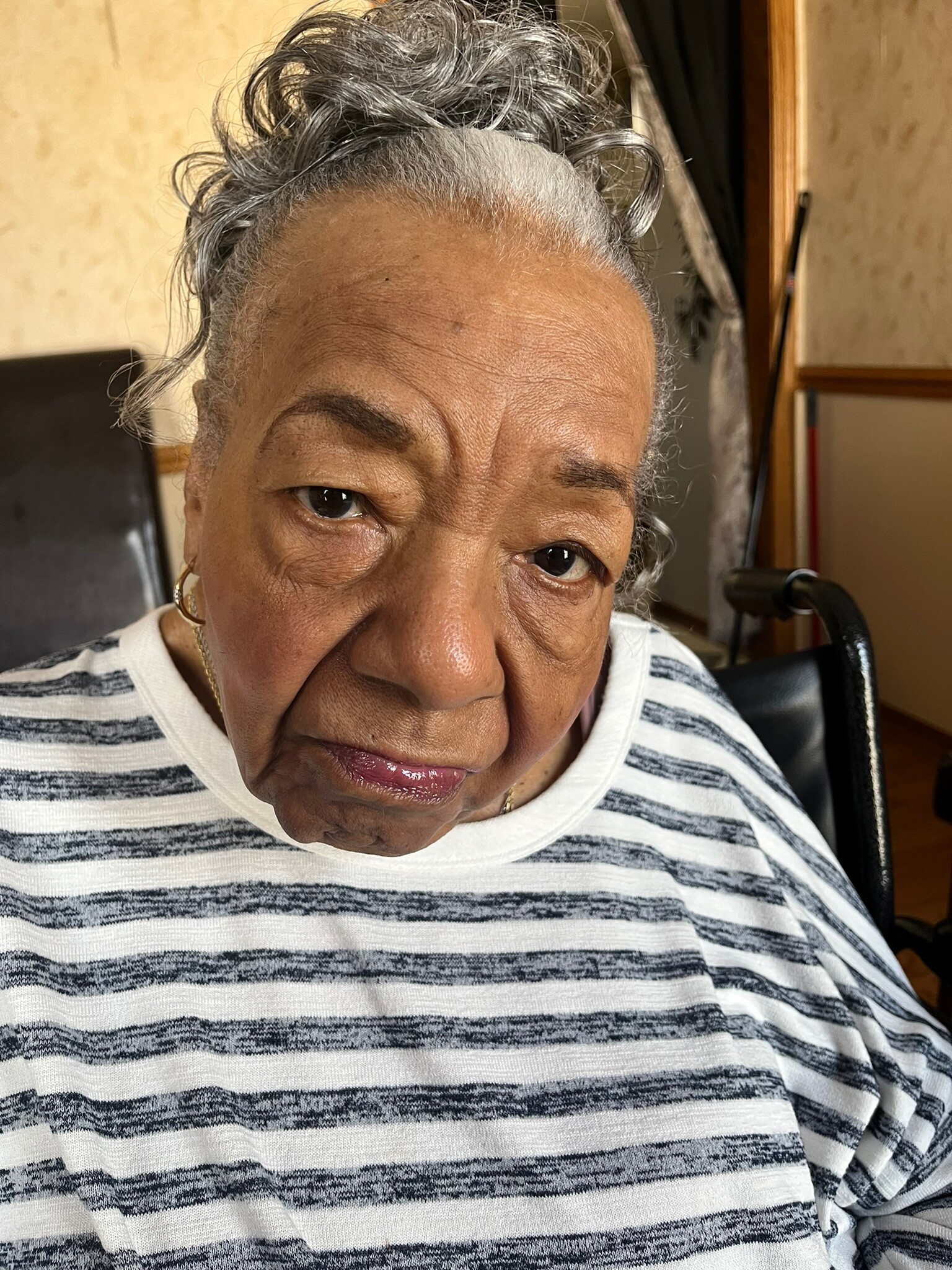 Close-up of an older woman looking slightly downward, with gray hair pulled back and wearing a striped shirt.