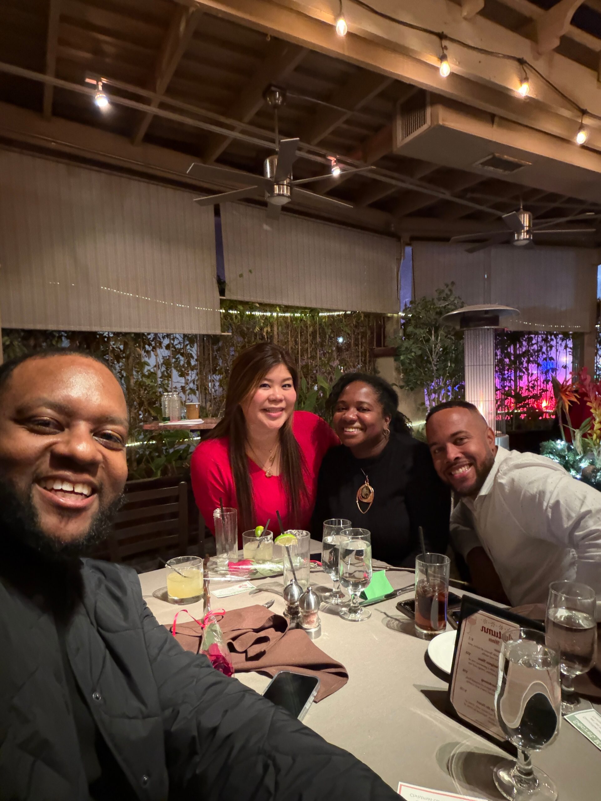 Four friends posing and smiling at a restaurant table with drinks and lime wedges in front of them.