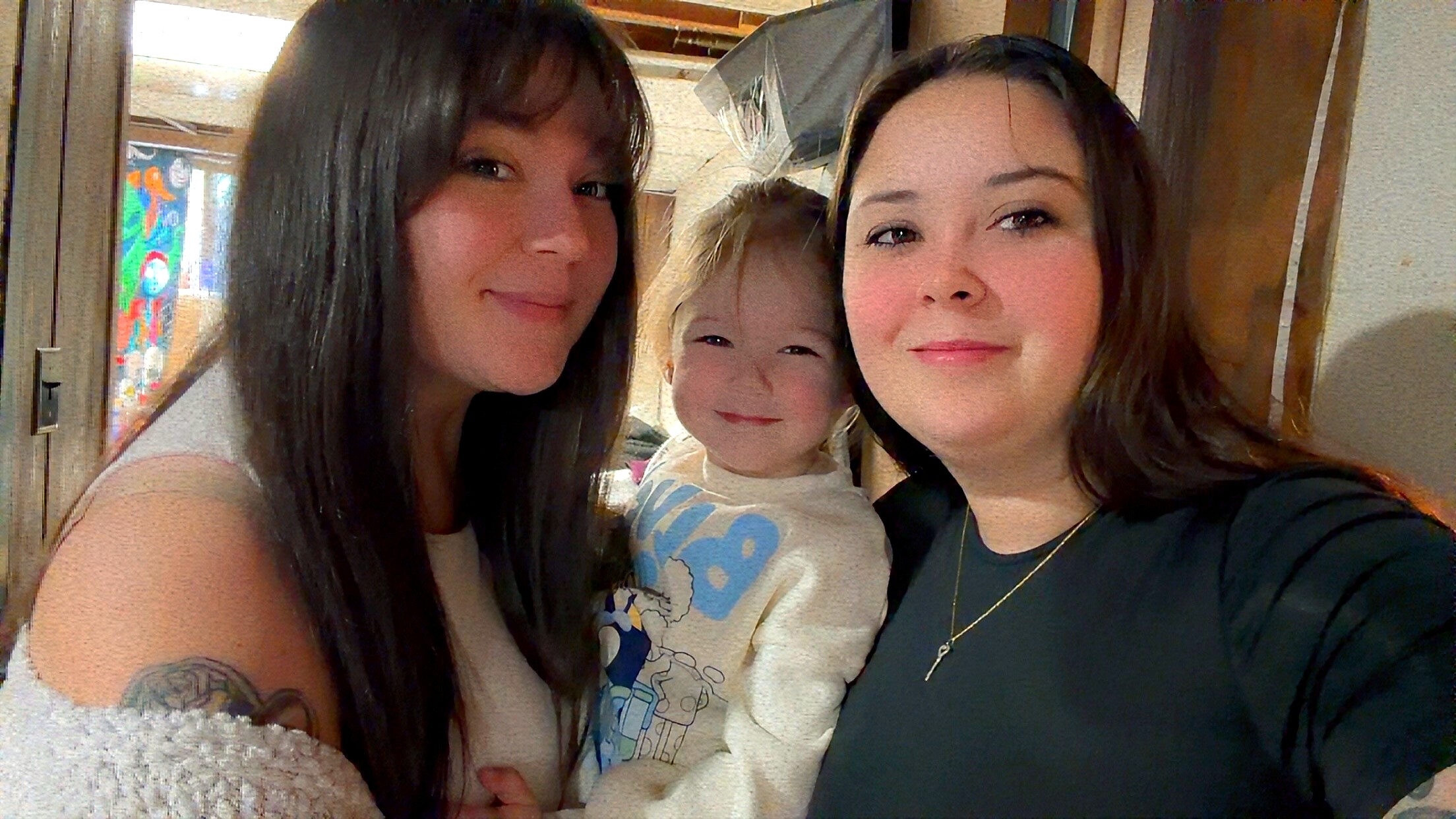 Three people posing for a close selfie indoors, two women on the sides and a child in the middle, all smiling. (informative)