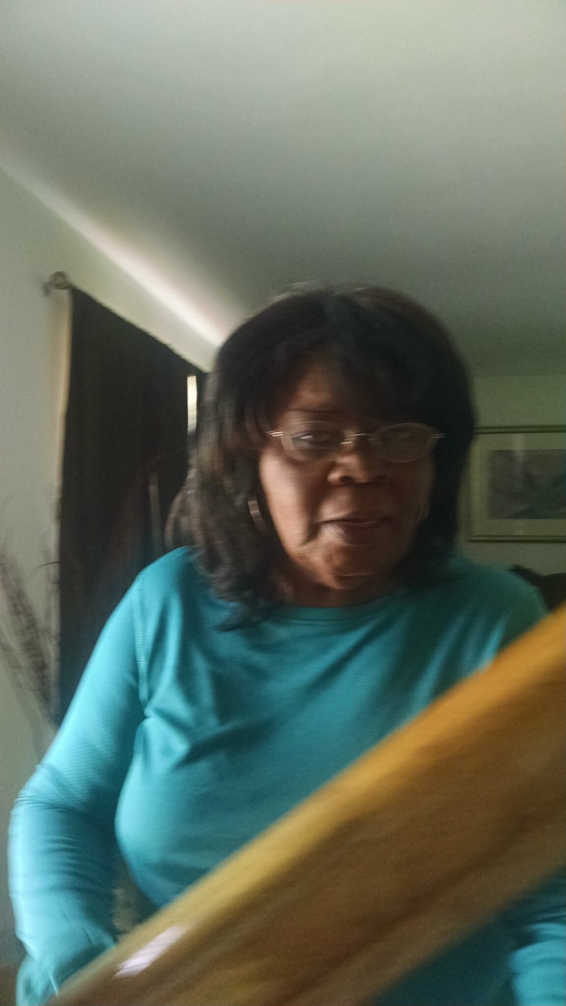 Smiling woman with glasses in a teal shirt indoors, captured in motion with a wooden railing across the foreground.