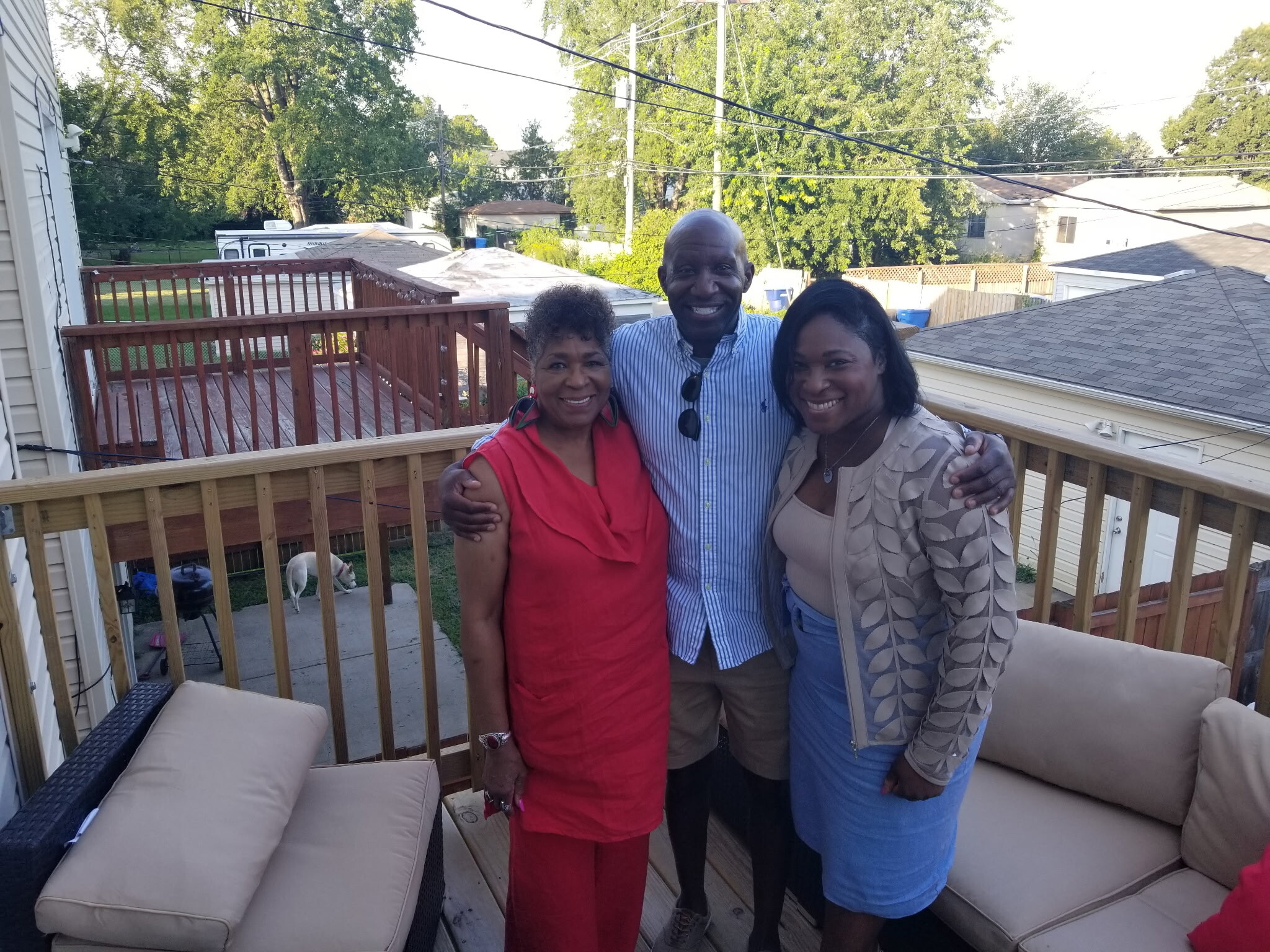 Three adults posing together on a wooden backyard deck, smiling at the camera.