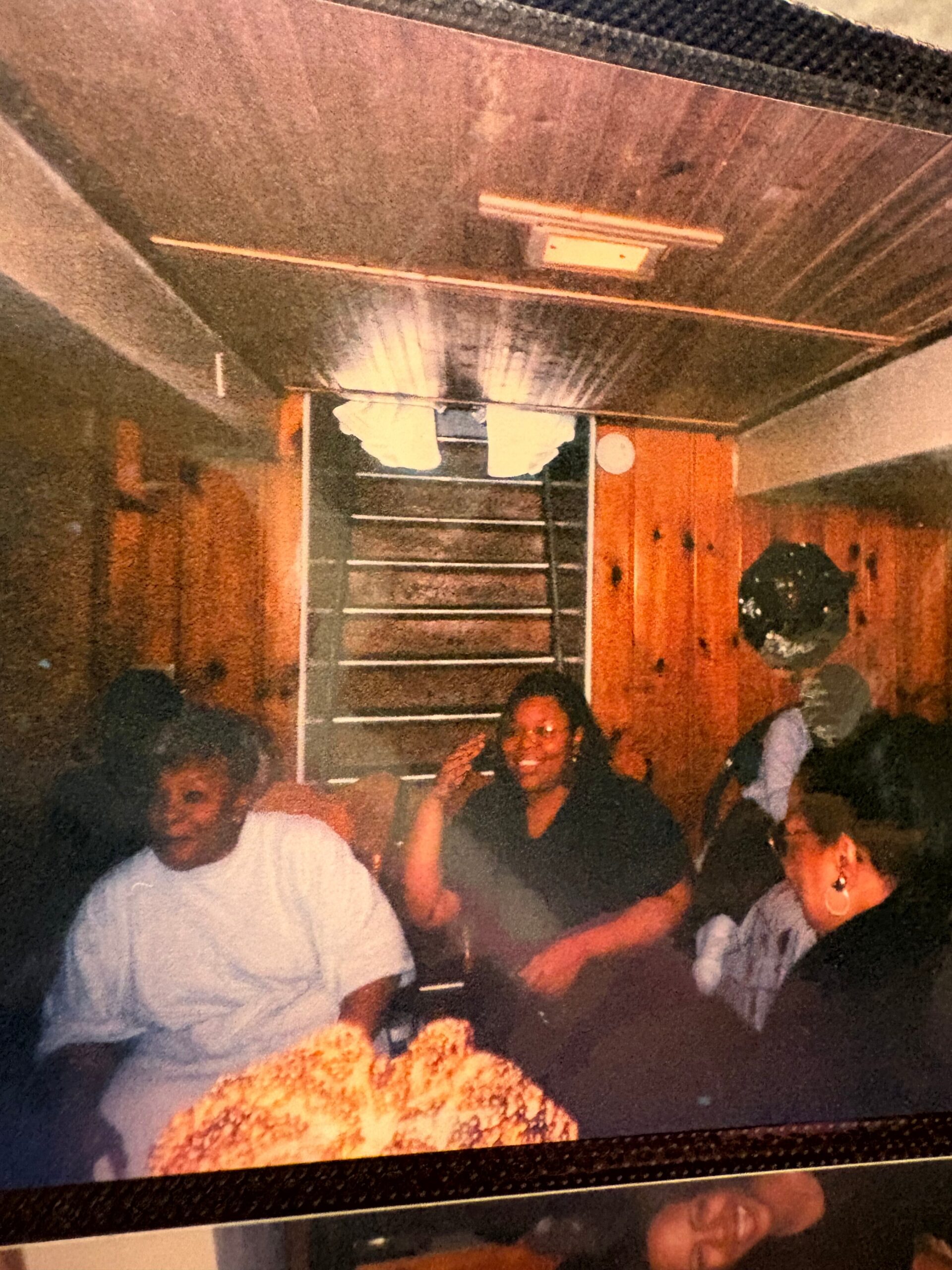People gathered around a table in a warm, wood-paneled room, smiling and posing for a casual group photo.