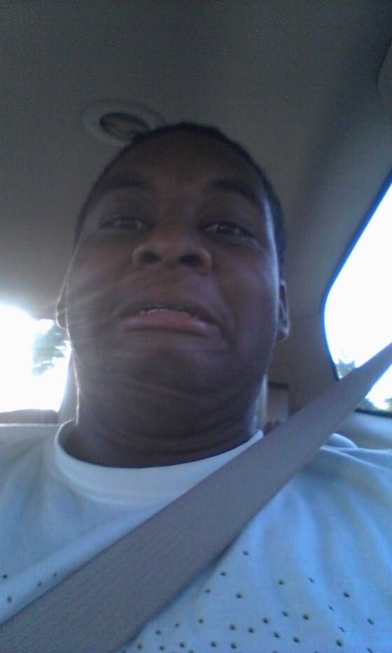 Close-up selfie of a man wearing a seatbelt inside a car, looking at the camera with a puckered expression.