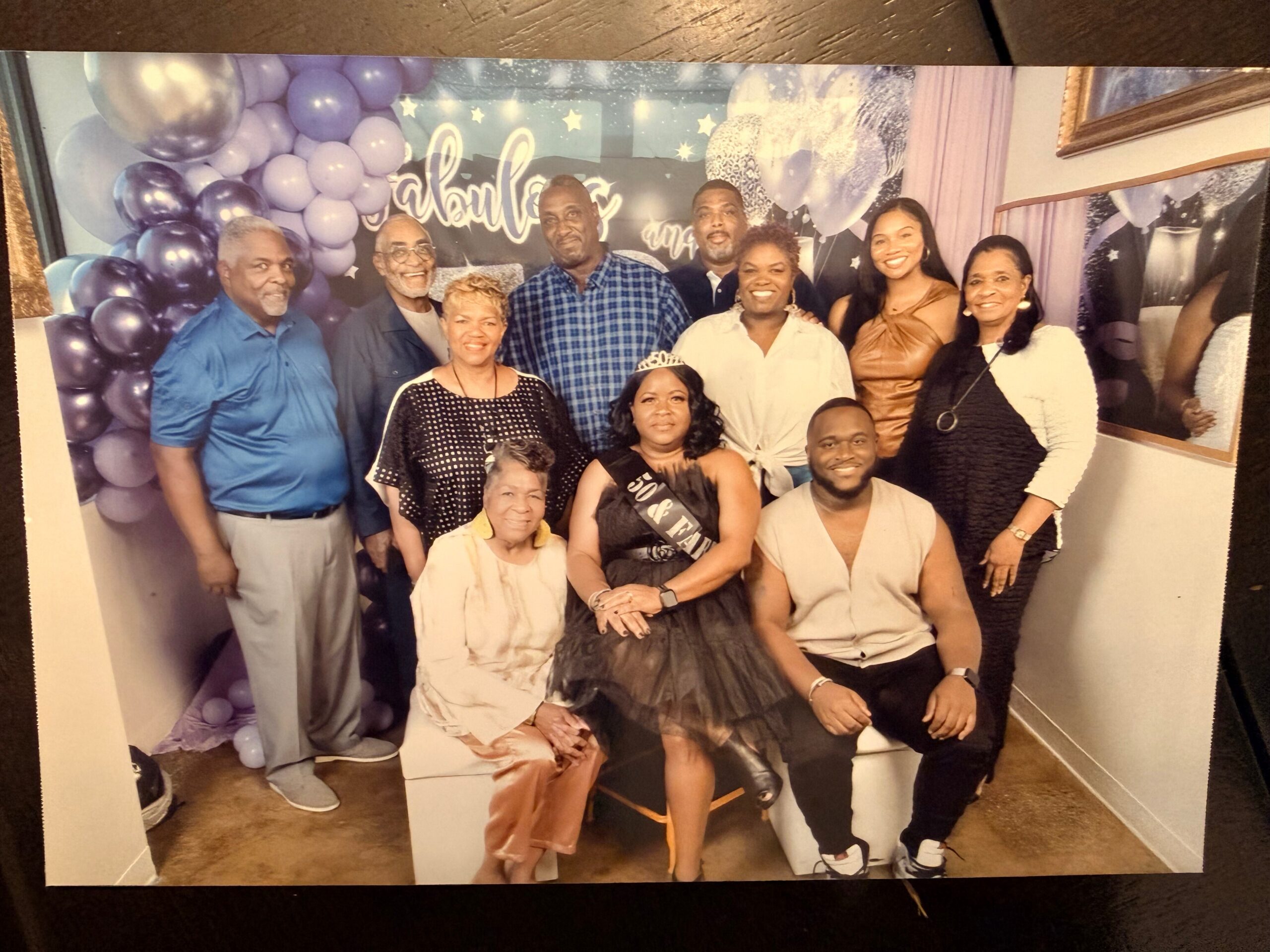 Group of adults posing and smiling at a celebration in front of a purple balloon wall backdrop with a starry banner behind them.