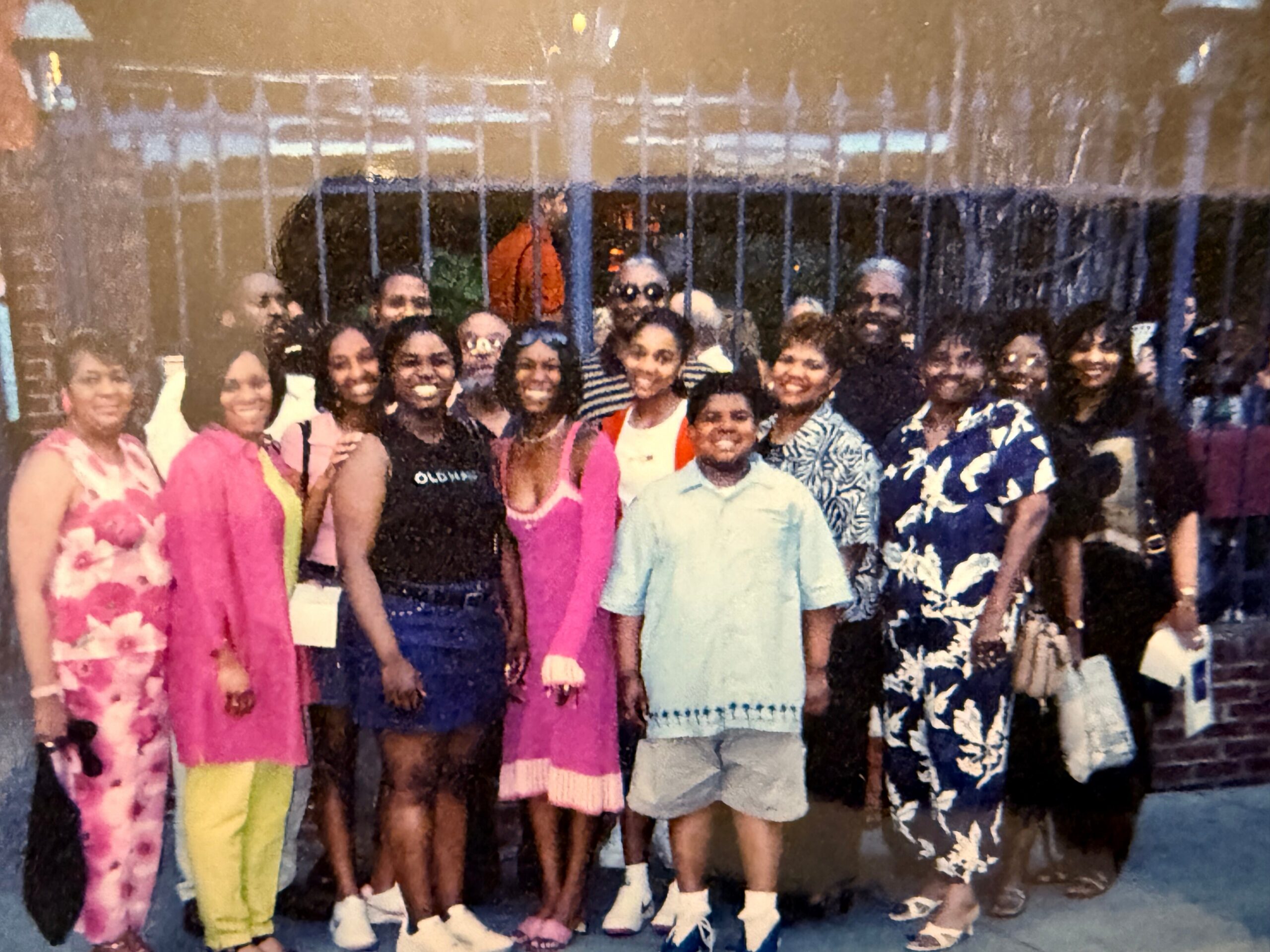 Group of people standing together for a outdoor group photo, smiling, wearing colorful clothes.