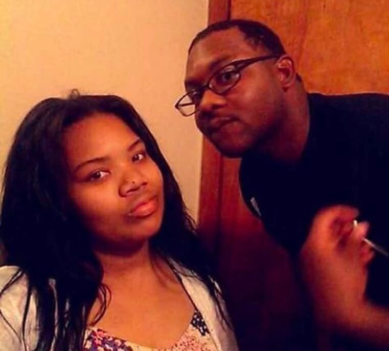 Two friends posing indoors for a photo: a woman with long dark hair on the left and a man with glasses on the right, both looking at the camera.
