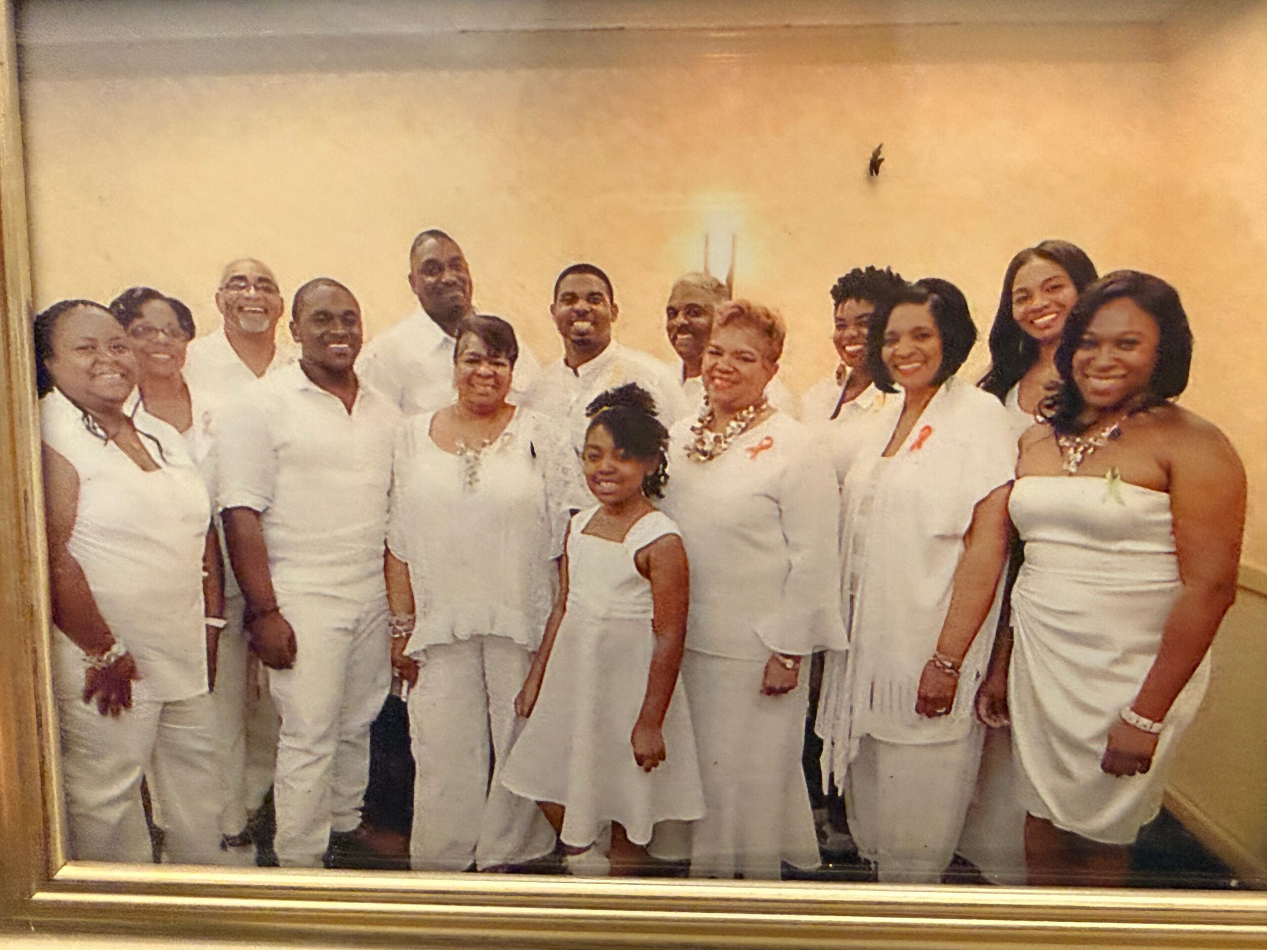 Group of people in white outfits posing together for a formal photo, inside a frame framing a framed group portrait.
