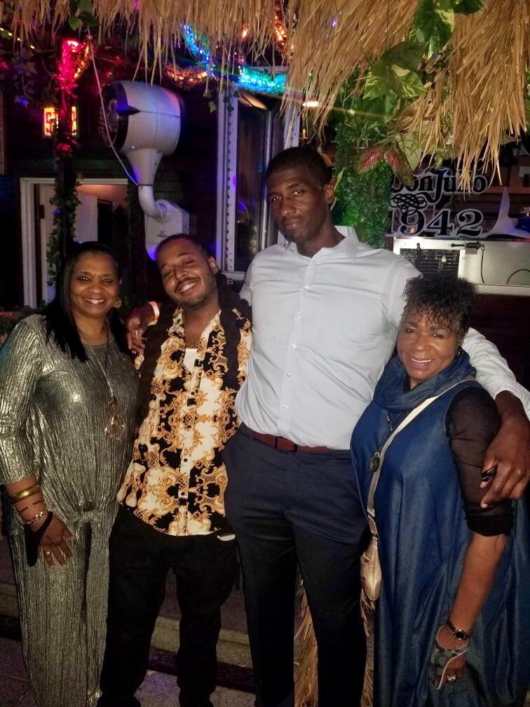 Four adults posing together at a lively night spot with colorful lights, smiling for the camera.