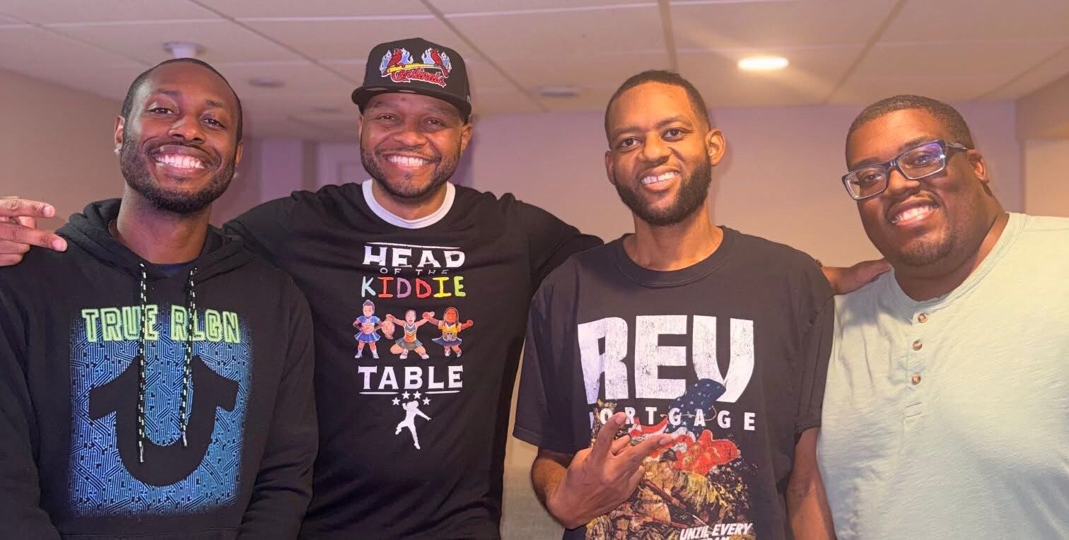 Four men posing together indoors, smiling at the camera.
