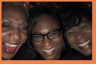 Three women smiling and leaning in for a selfie at a social gathering, frames of their faces close together and joyful expressions.