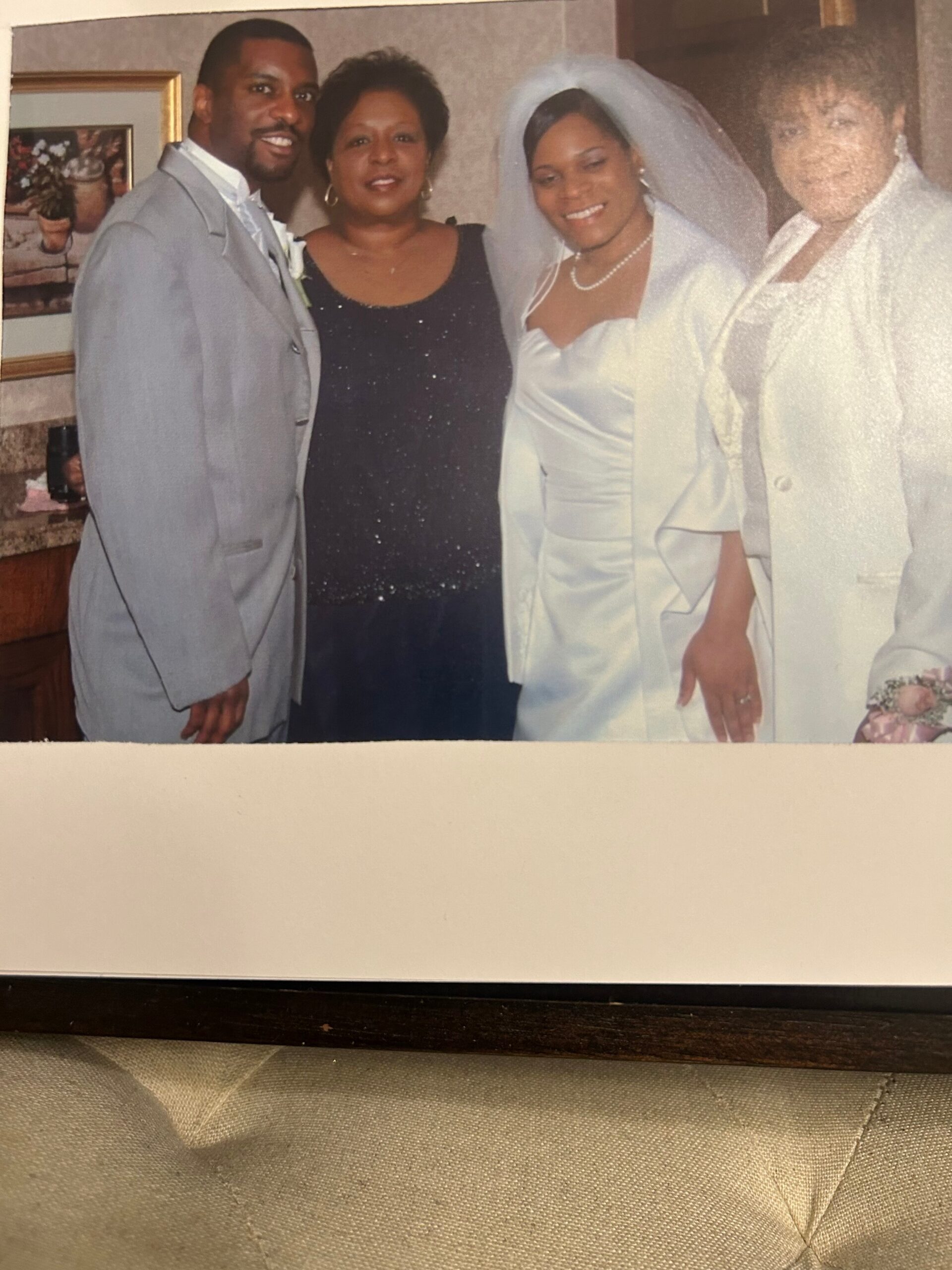 Wedding party posing indoors: groom in a gray suit, bride in a white gown and veil, with two women in dark and light dresses.
