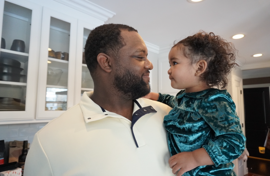 Father holding his young daughter and sharing a smile in a bright kitchen.