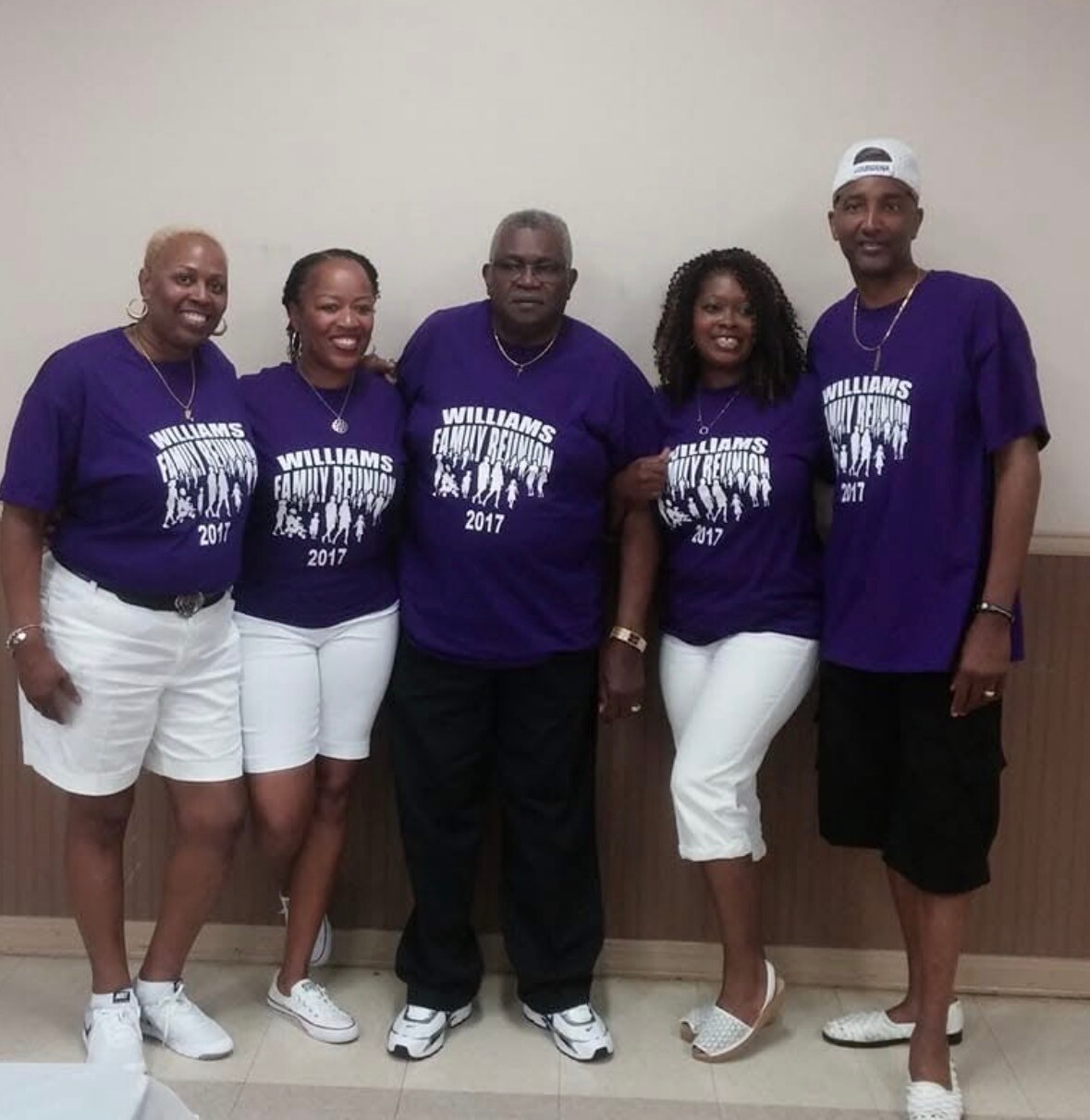 Five adults wearing matching purple Williams Family Reunion 2017 shirts stand together indoors, smiling for a group photo.