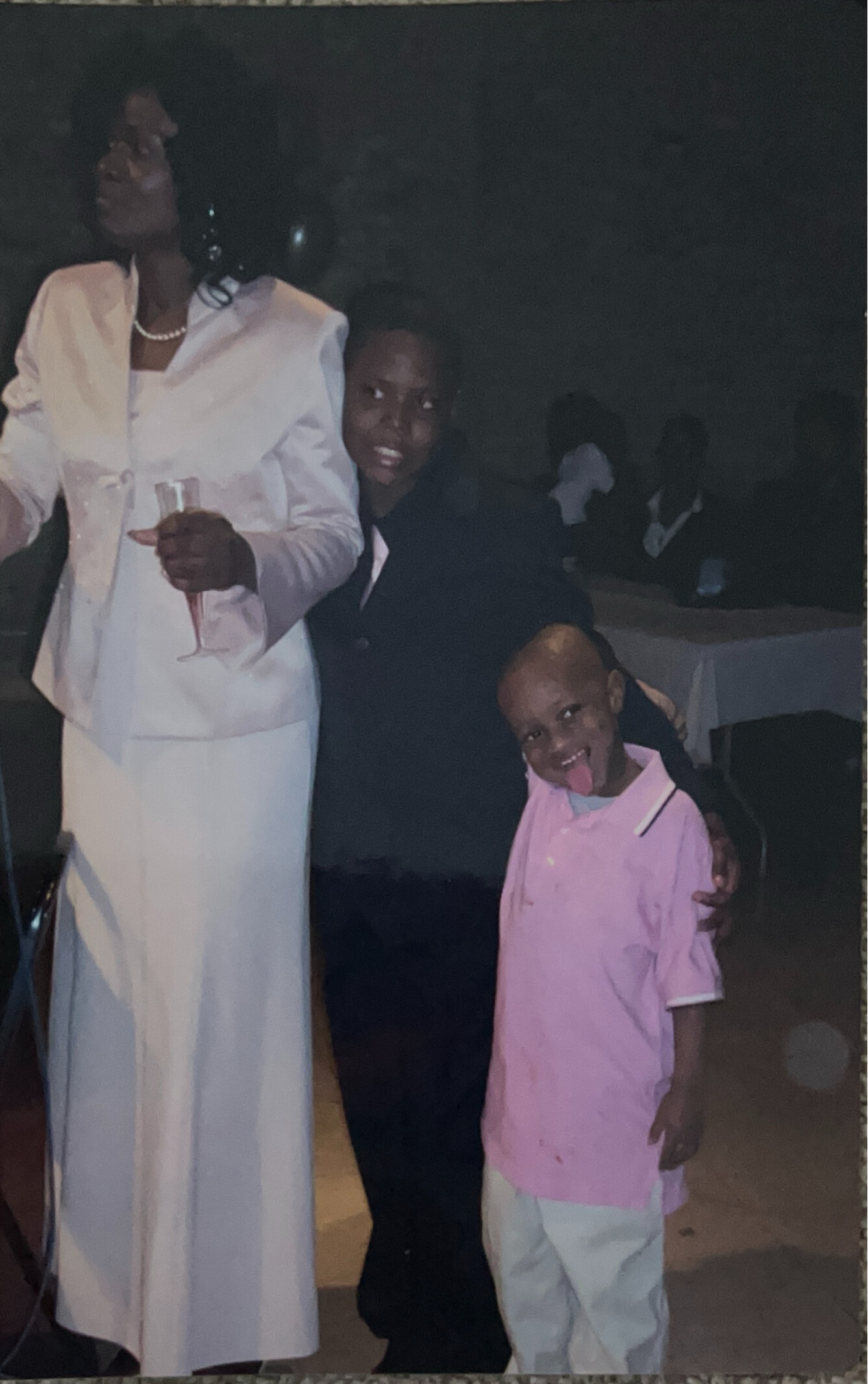 Woman in a white suit with a pearl necklace holding a champagne flute, posing with a smiling child in pink at a nighttime gathering.