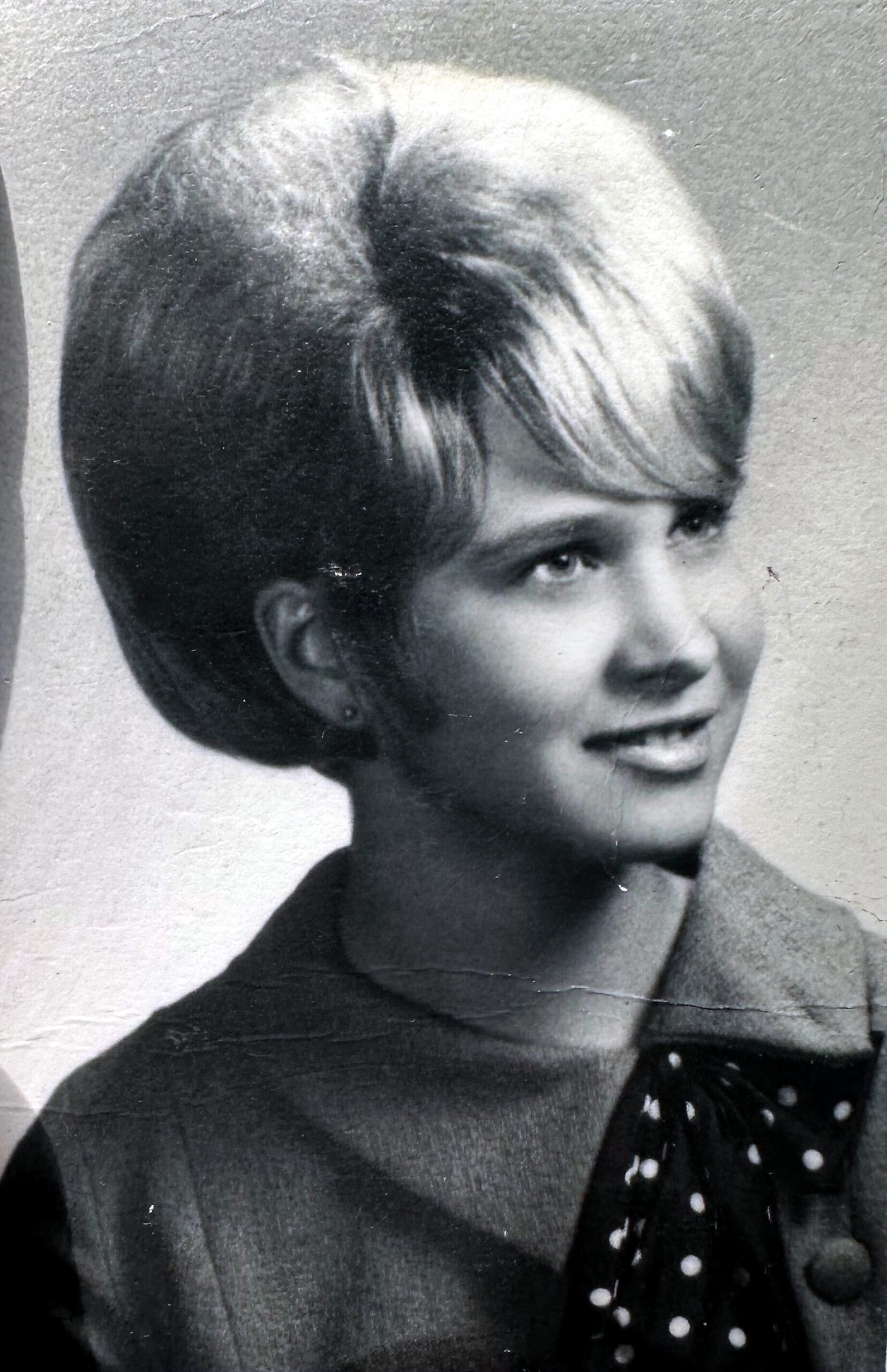 Black-and-white portrait of a young woman with short hair, wearing a dark sweater and a polka-dot scarf, looking to the right.